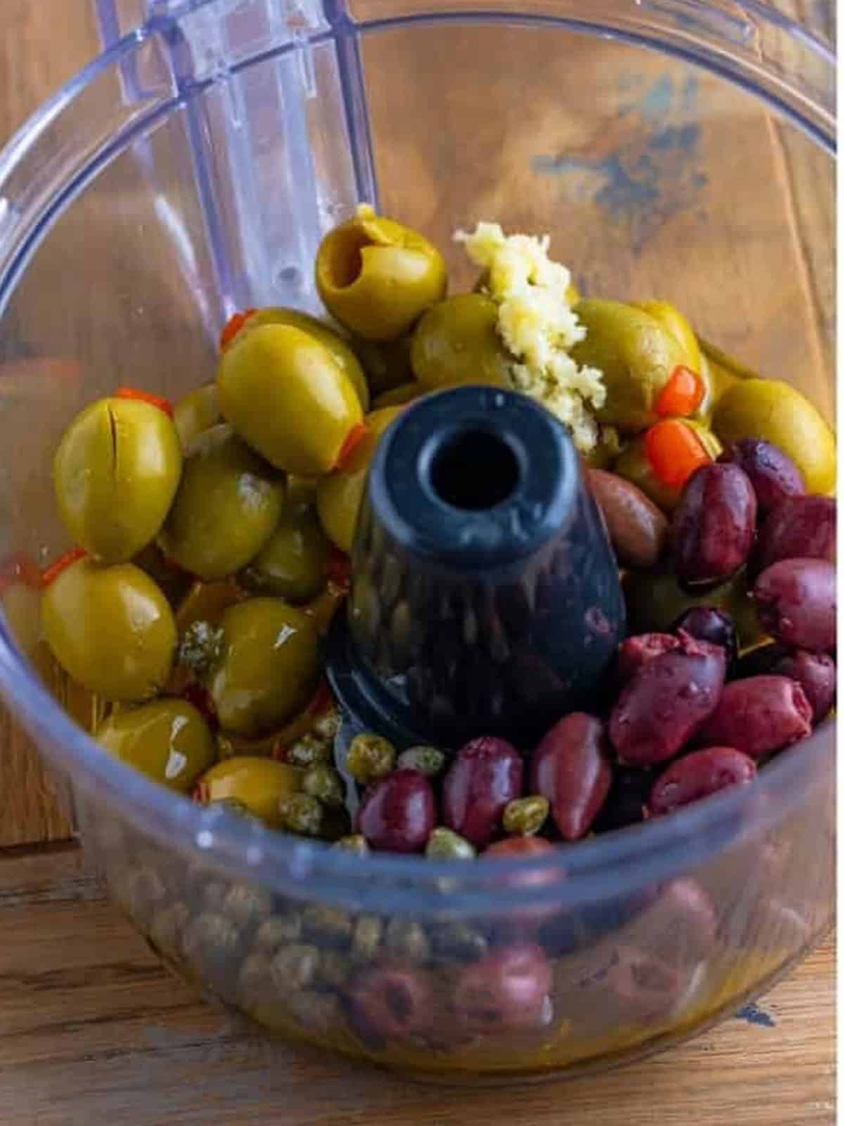 Green olives, kalamata olives, capers, garlic, and lemon juice in a food processor for olive tapenade recipe.