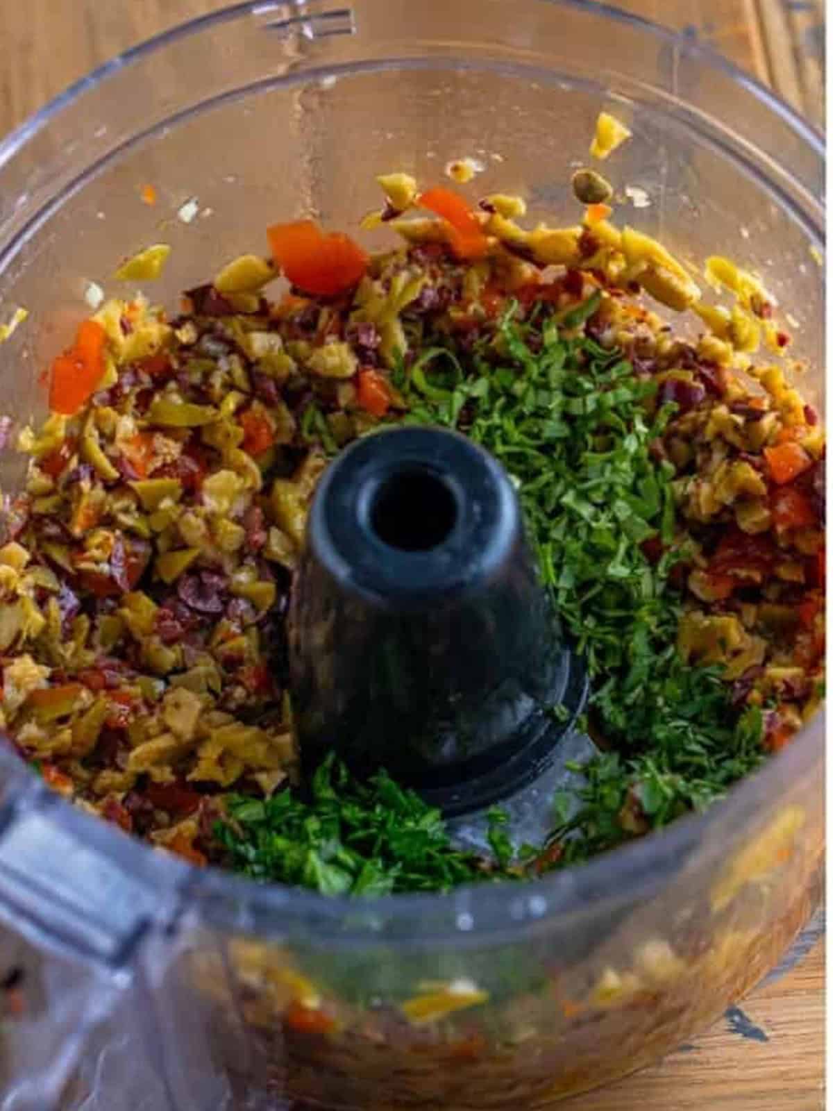 Fresh parsley, basil, and oregano added on top of chopped olives in the food processor for olive tapenade.