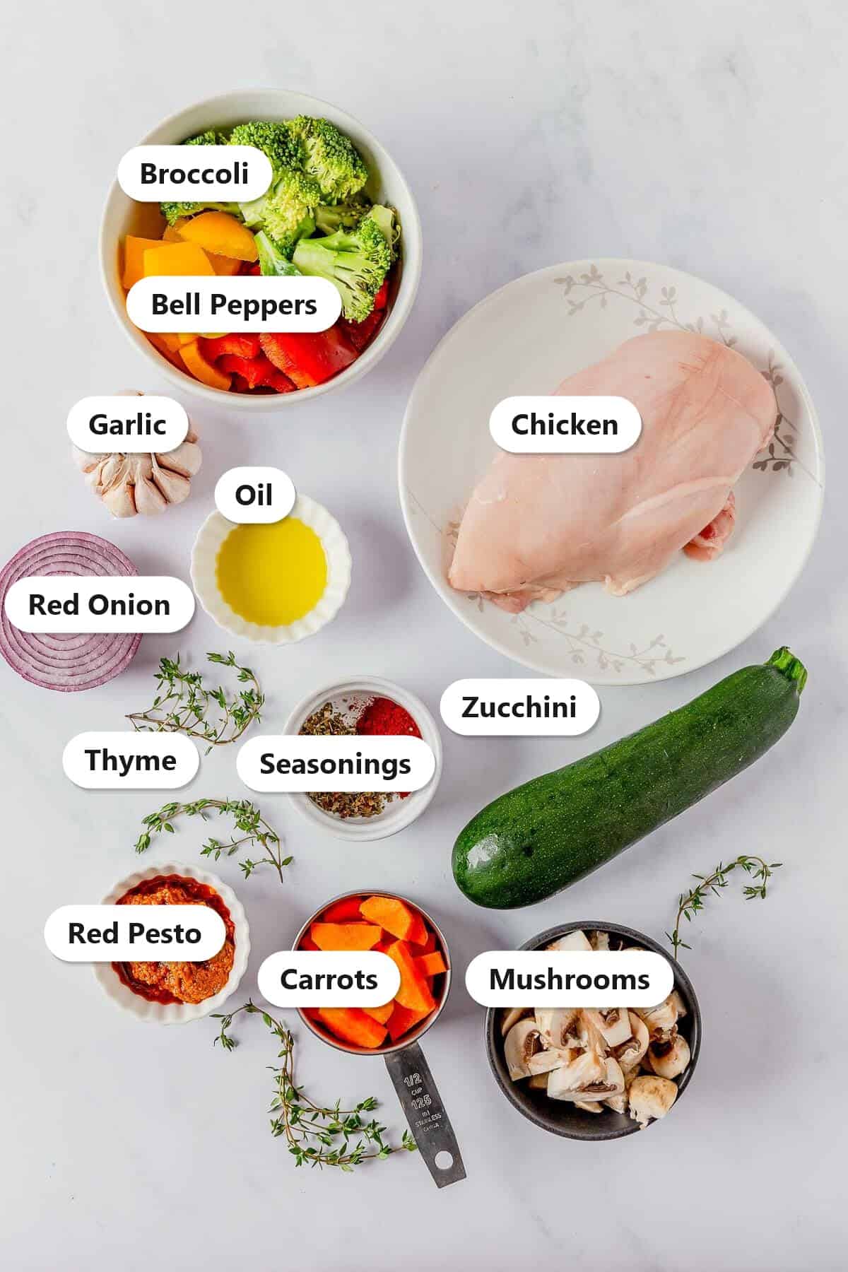 Labeled ingredients for one pan chicken and vegetables including chicken, bell peppers, broccoli, zucchini, mushrooms, carrots, and red pesto.