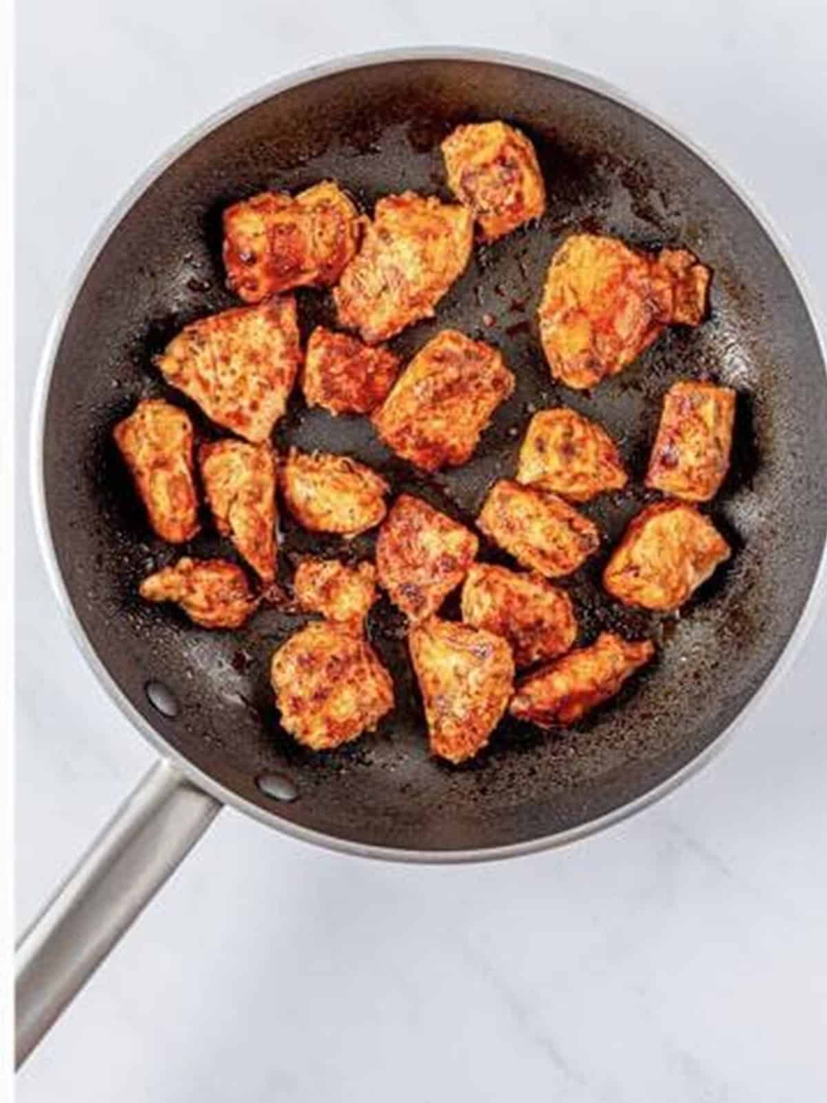 Seasoned chicken pieces cooking in a skillet until golden.