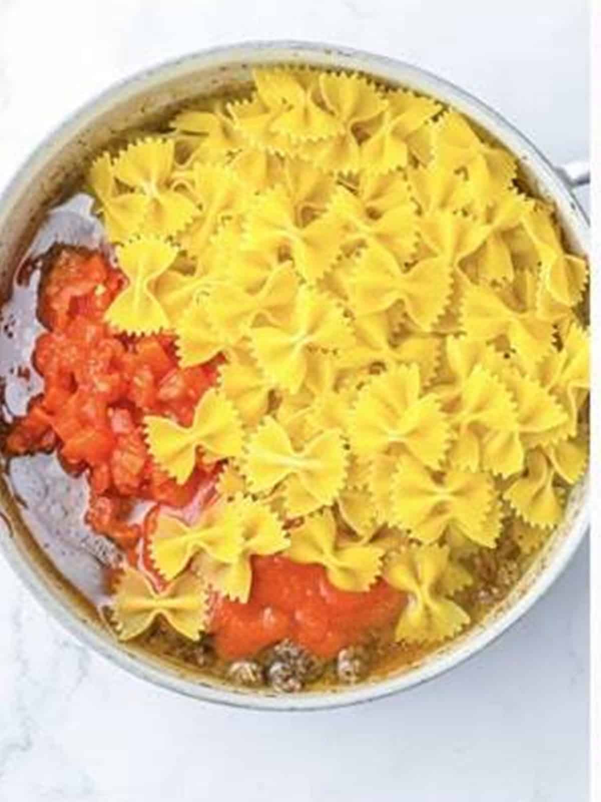 Bowtie pasta and diced tomatoes added to a skillet for one pot lasagna.