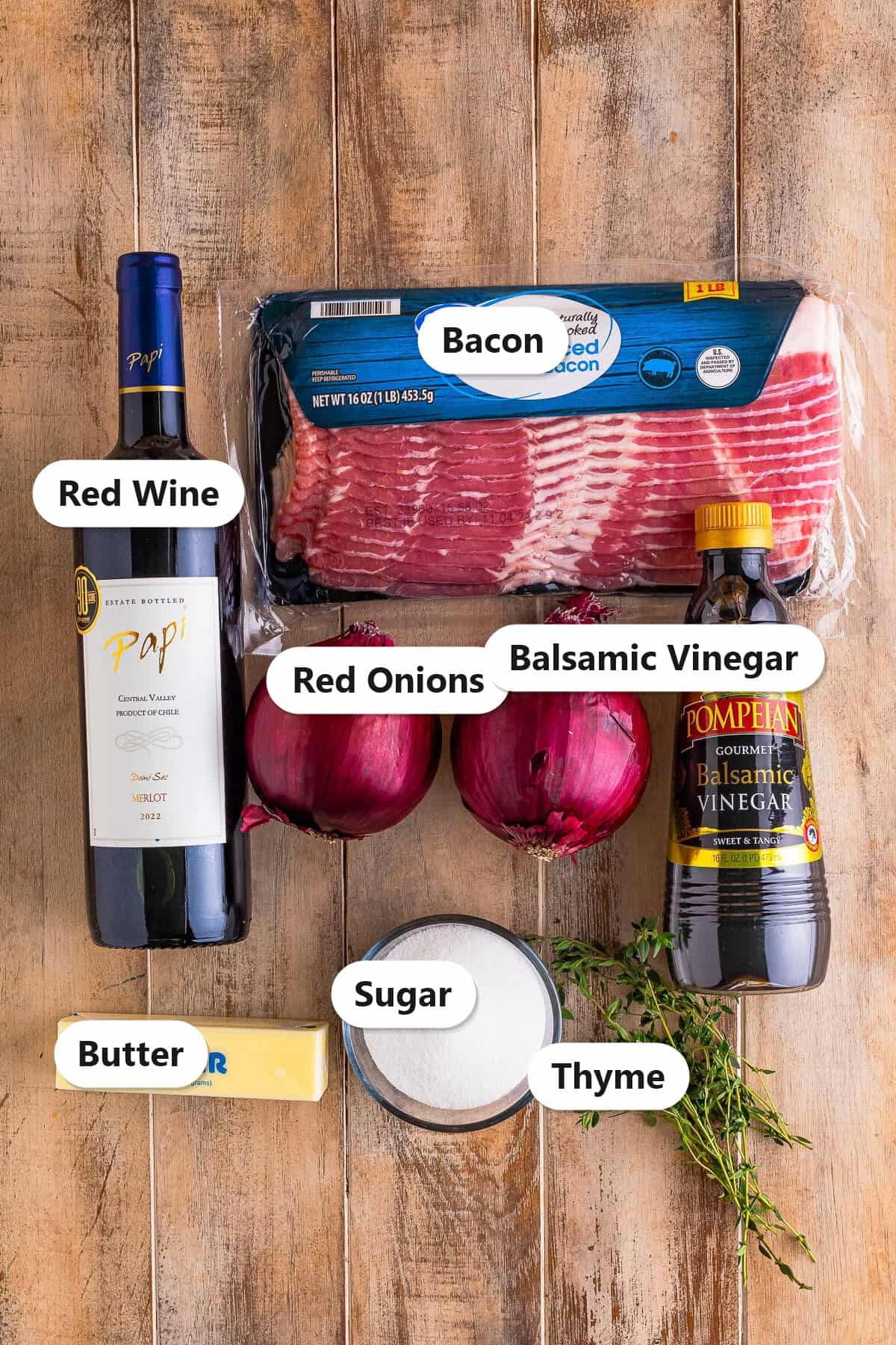 Labeled ingredients to make onion marmalade including red wine, bacon, red onions, balsamic vinegar, sugar, butter, and thyme.