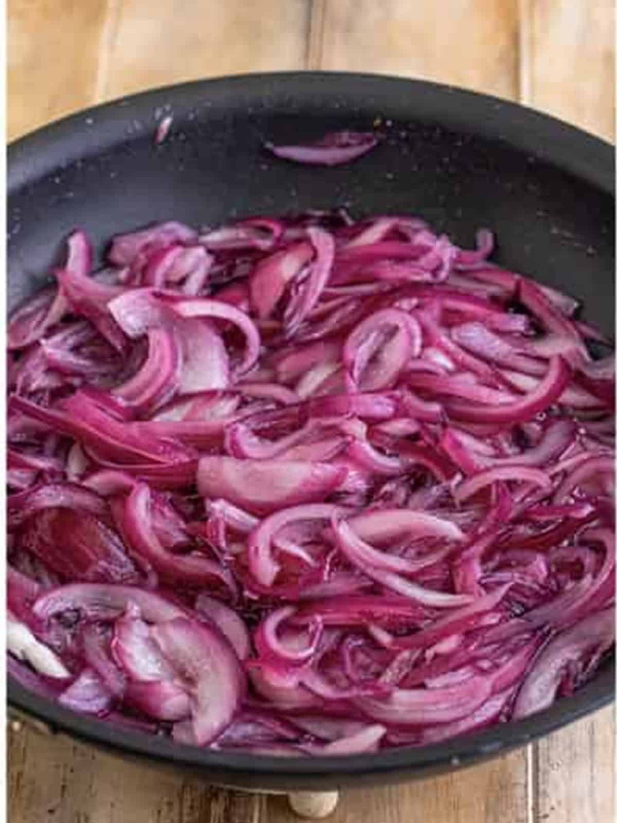 Red onions softening and starting to caramelize in a skillet.