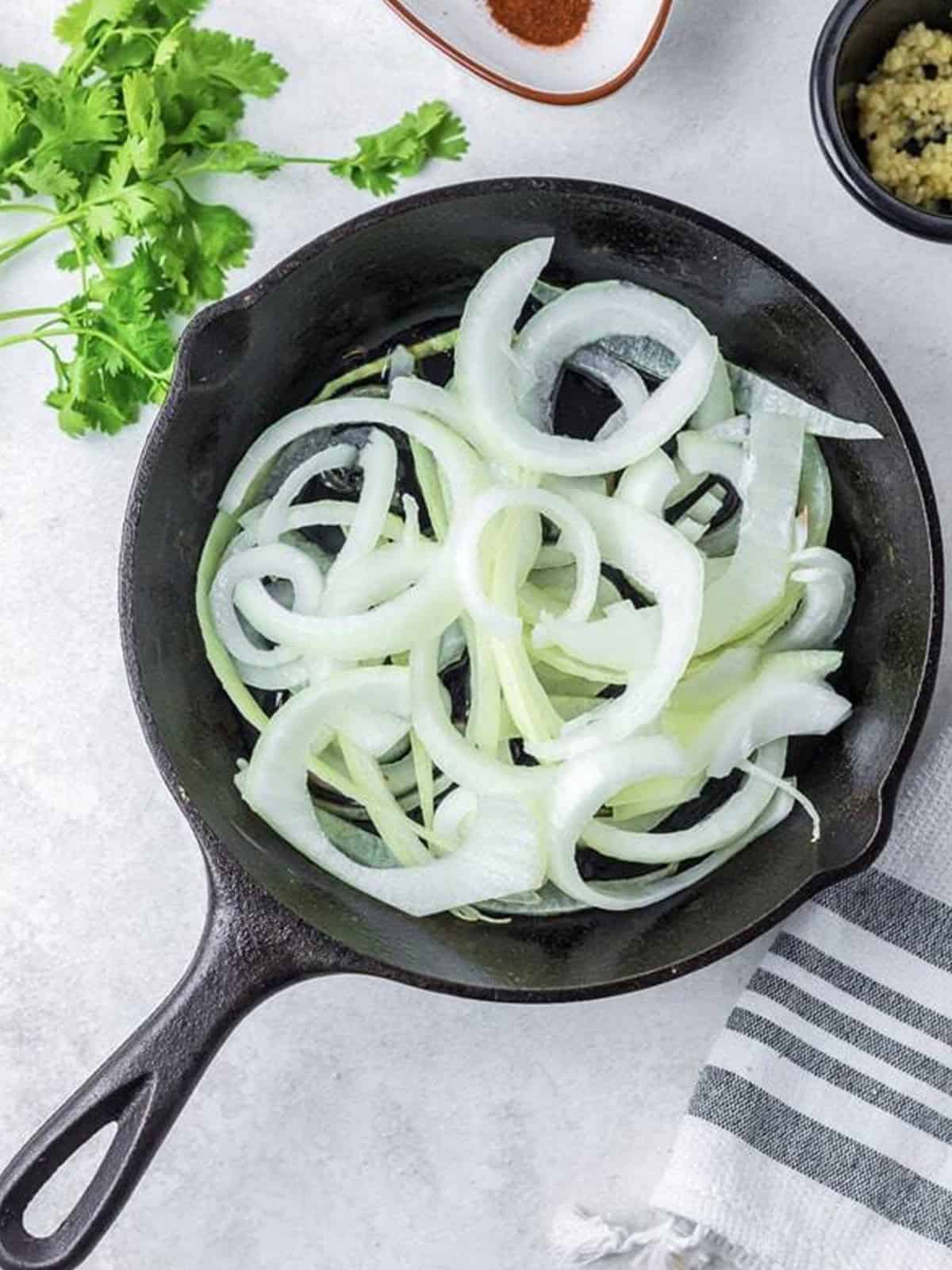 Sauteing sliced yellow onion rings in olive oil in a skillet.