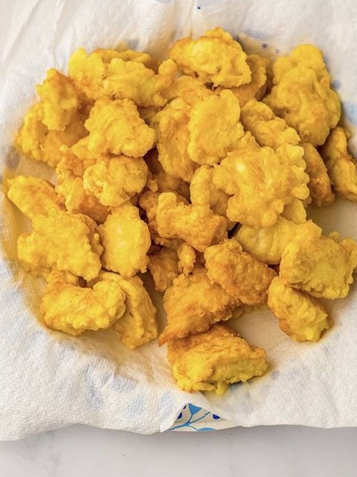 Golden fried chicken pieces draining on a paper towel.
