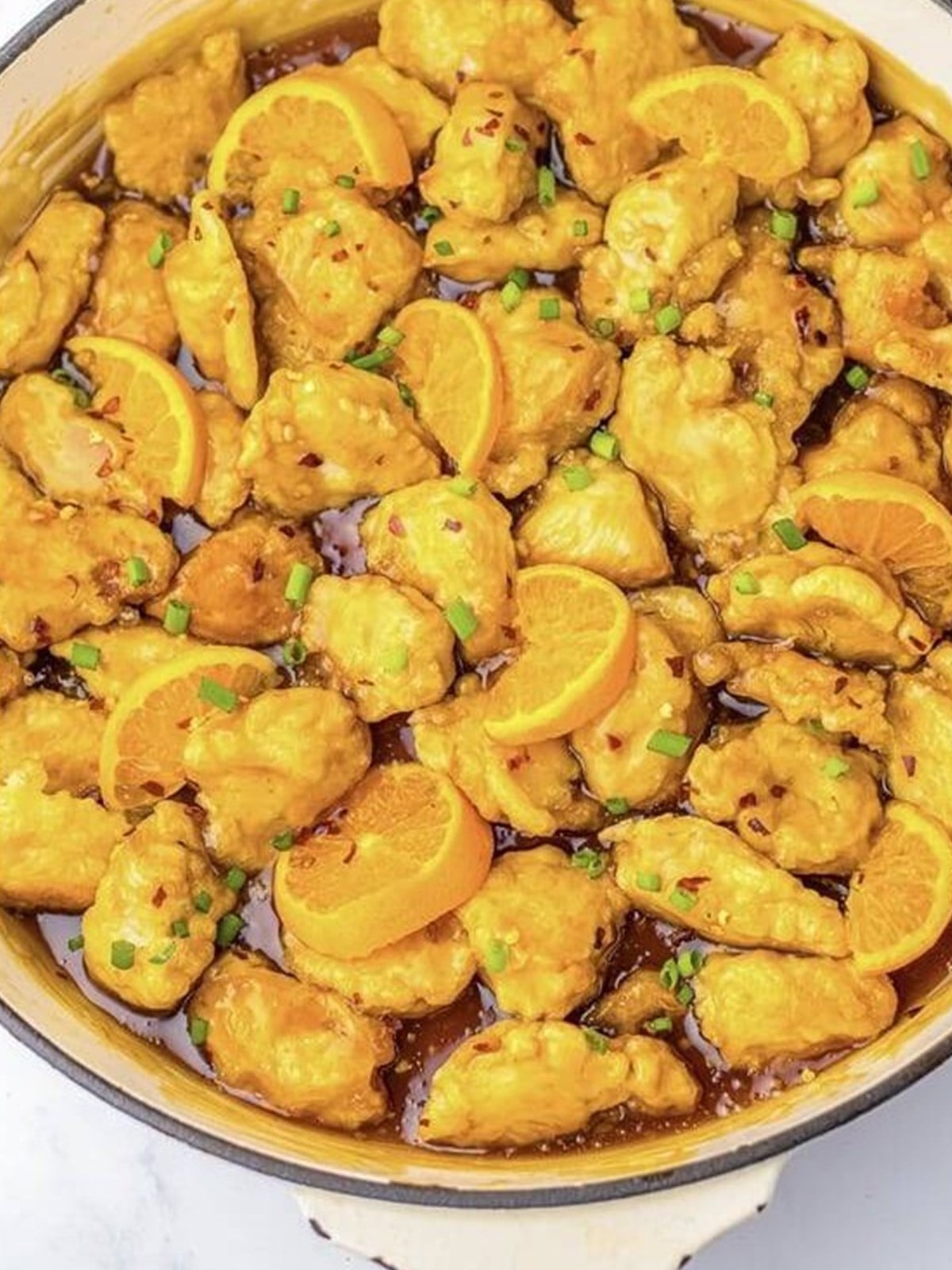 Fried chicken tossed in glossy orange sauce in a skillet.