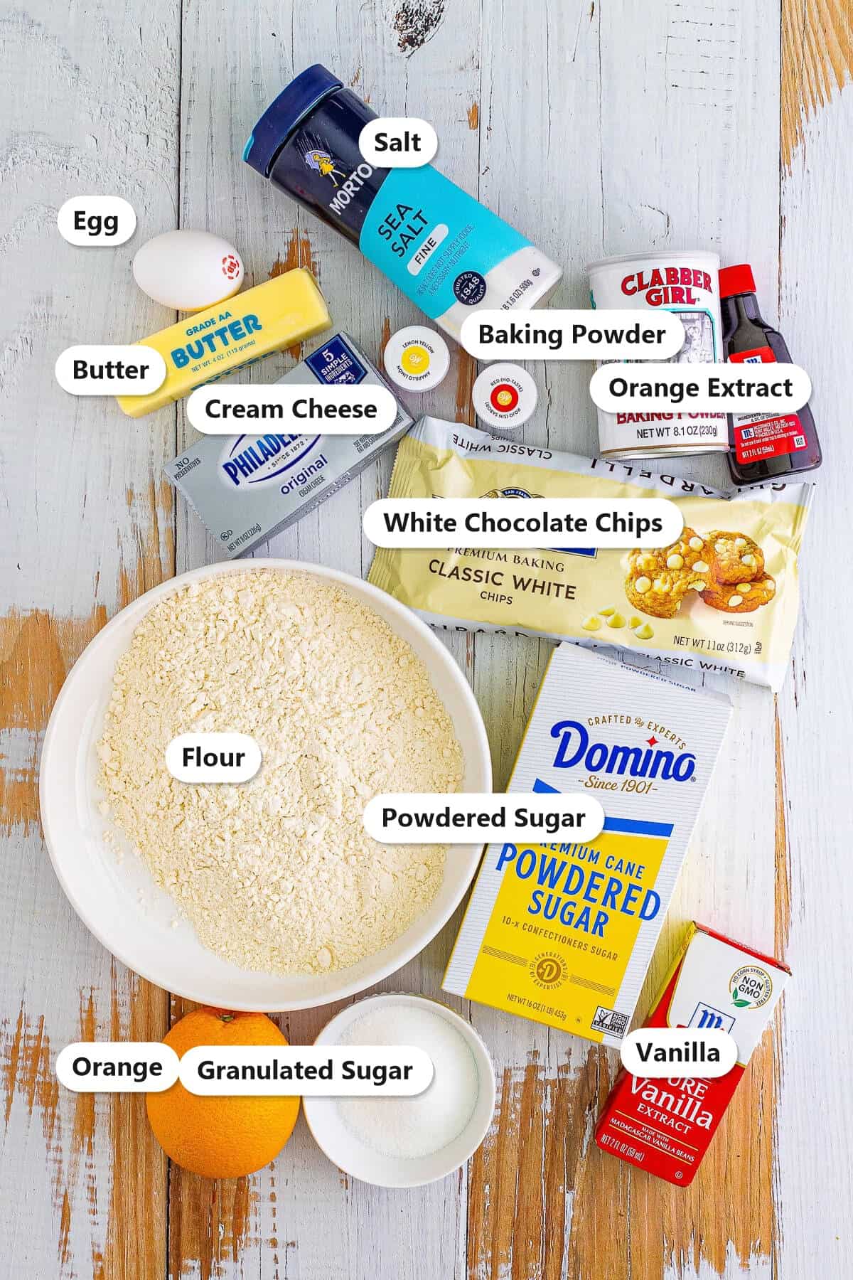 Labeled ingredients for orange creamsicle cookies including butter, cream cheese, powdered sugar, egg, orange, white chocolate chips, flour, baking powder, orange extract, vanilla, salt, and granulated sugar.