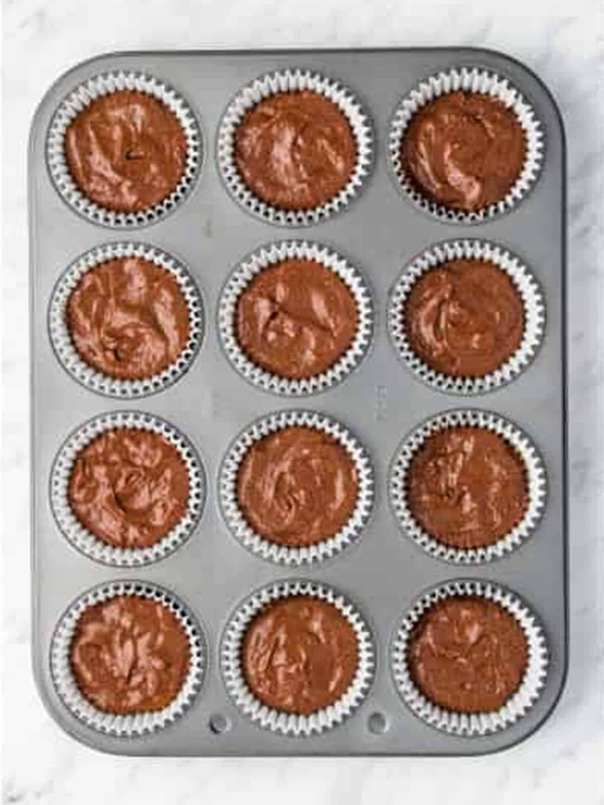 Chocolate cupcake batter divided into a lined muffin pan.