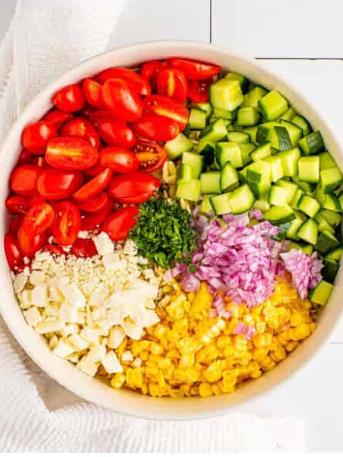 Orzo with tomatoes cucumber corn feta and onion in a bowl