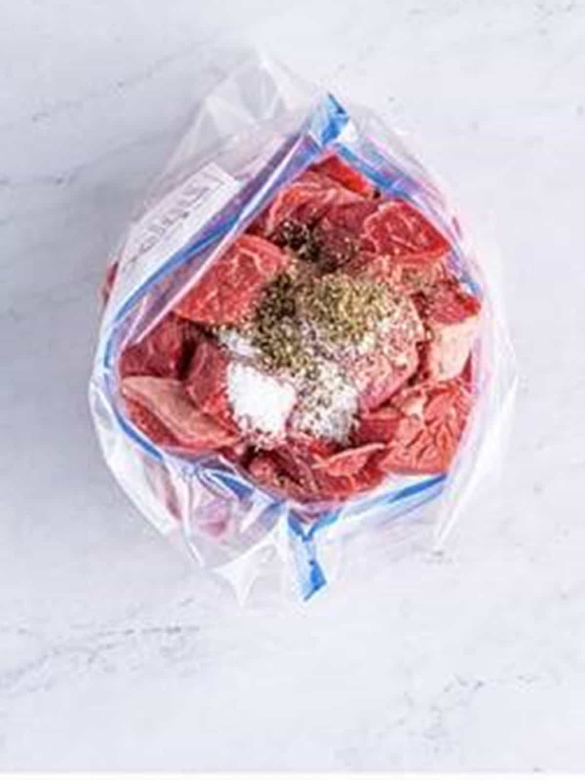 Chuck roast pieces in a zippered bag with salt and pepper for beef stew in the oven.