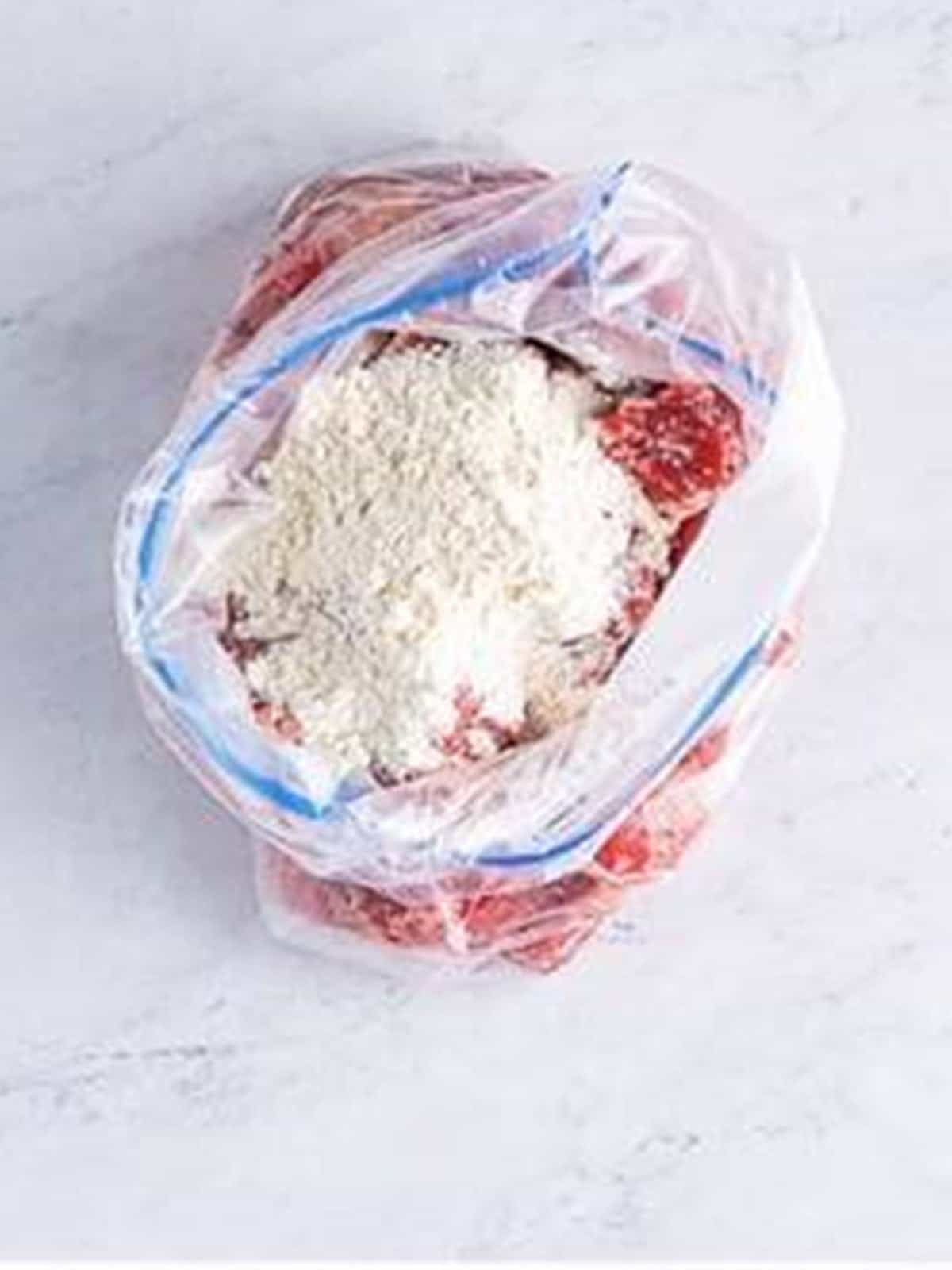 Flour added to the seasoned beef in a zippered bag for oven beef stew.