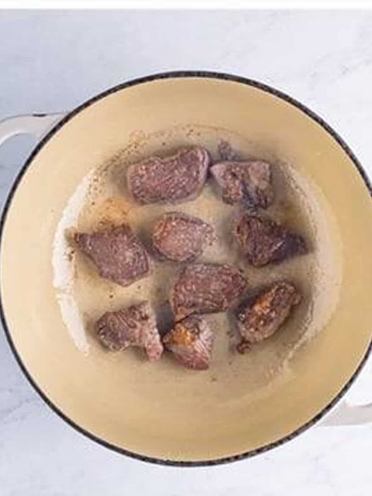 Floured chuck roast pieces searing in batches in a Dutch oven.