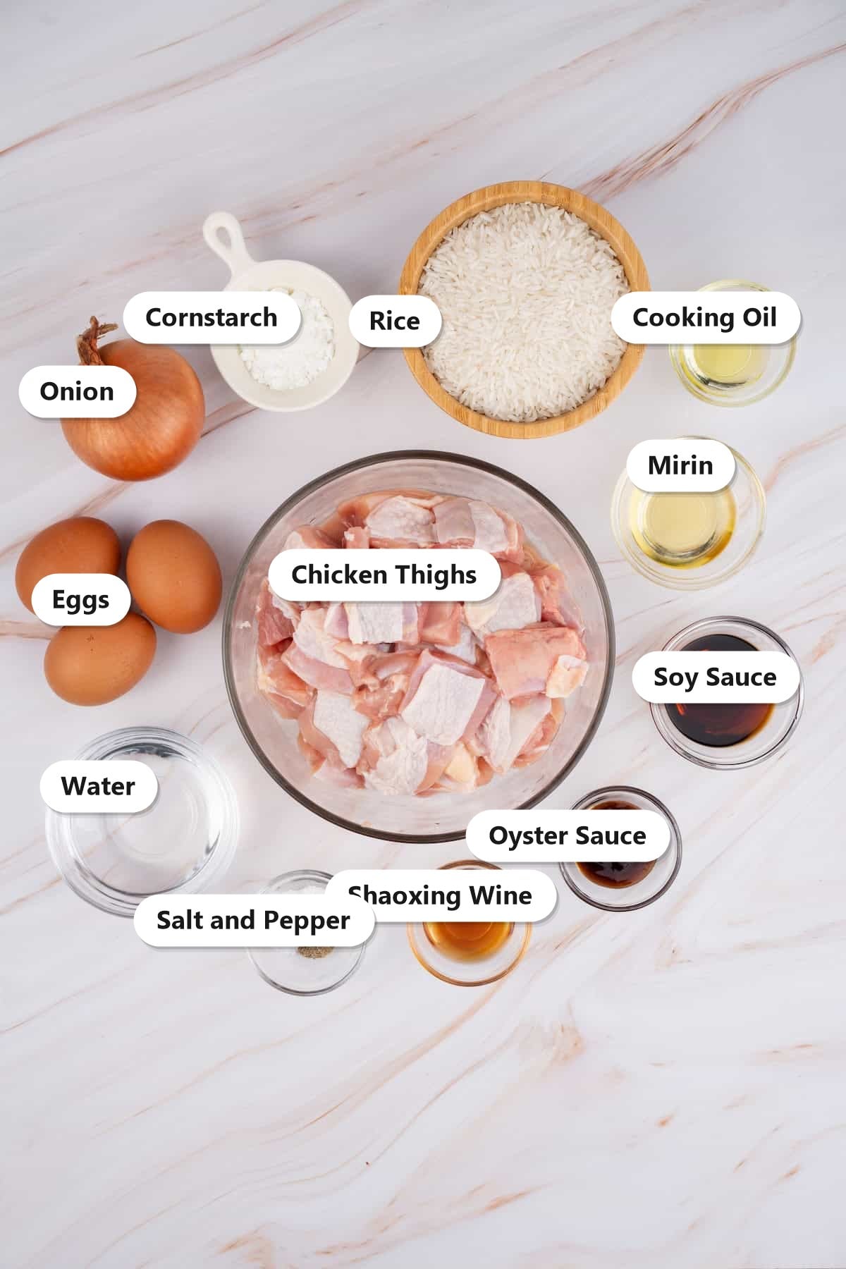 Labeled ingredients to make oyakodon including chicken thighs, eggs, onion, rice, soy sauce, oyster sauce, mirin, Shaoxing wine, cornstarch, and cooking oil.