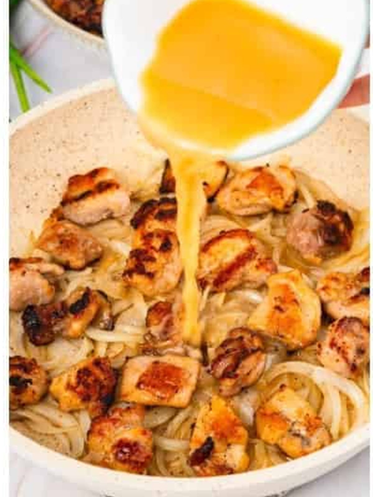 Beaten eggs being poured over the chicken and onion in the pan.