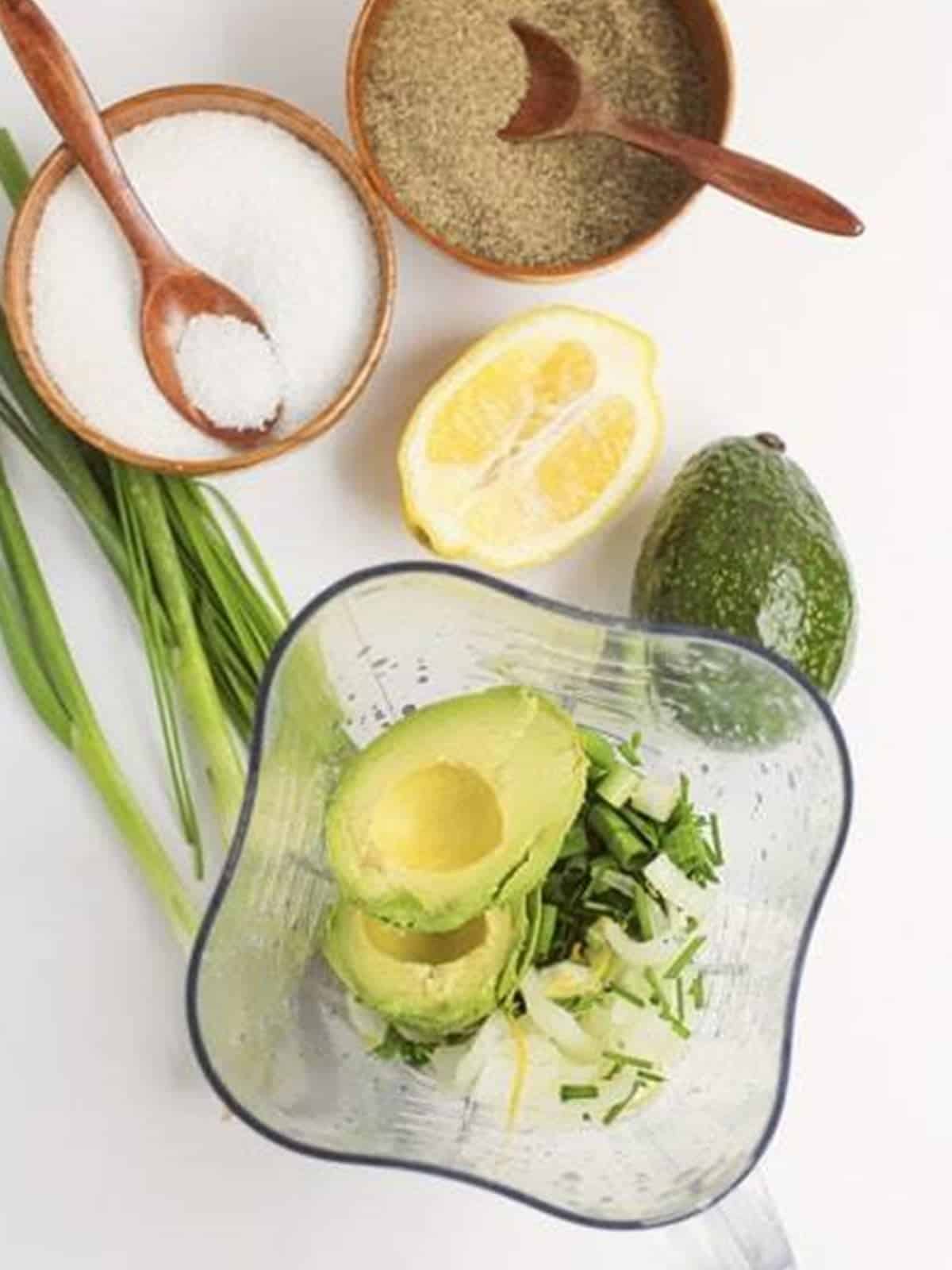 Avocado, herbs, and dressing ingredients added to a blender for green goddess dressing.