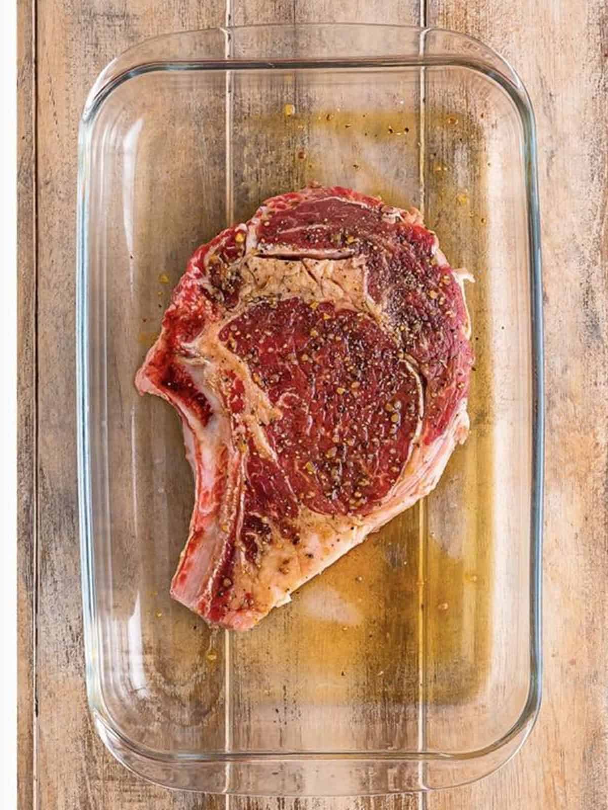 Bone-in ribeye steak marinating with Worcestershire sauce in a dish.