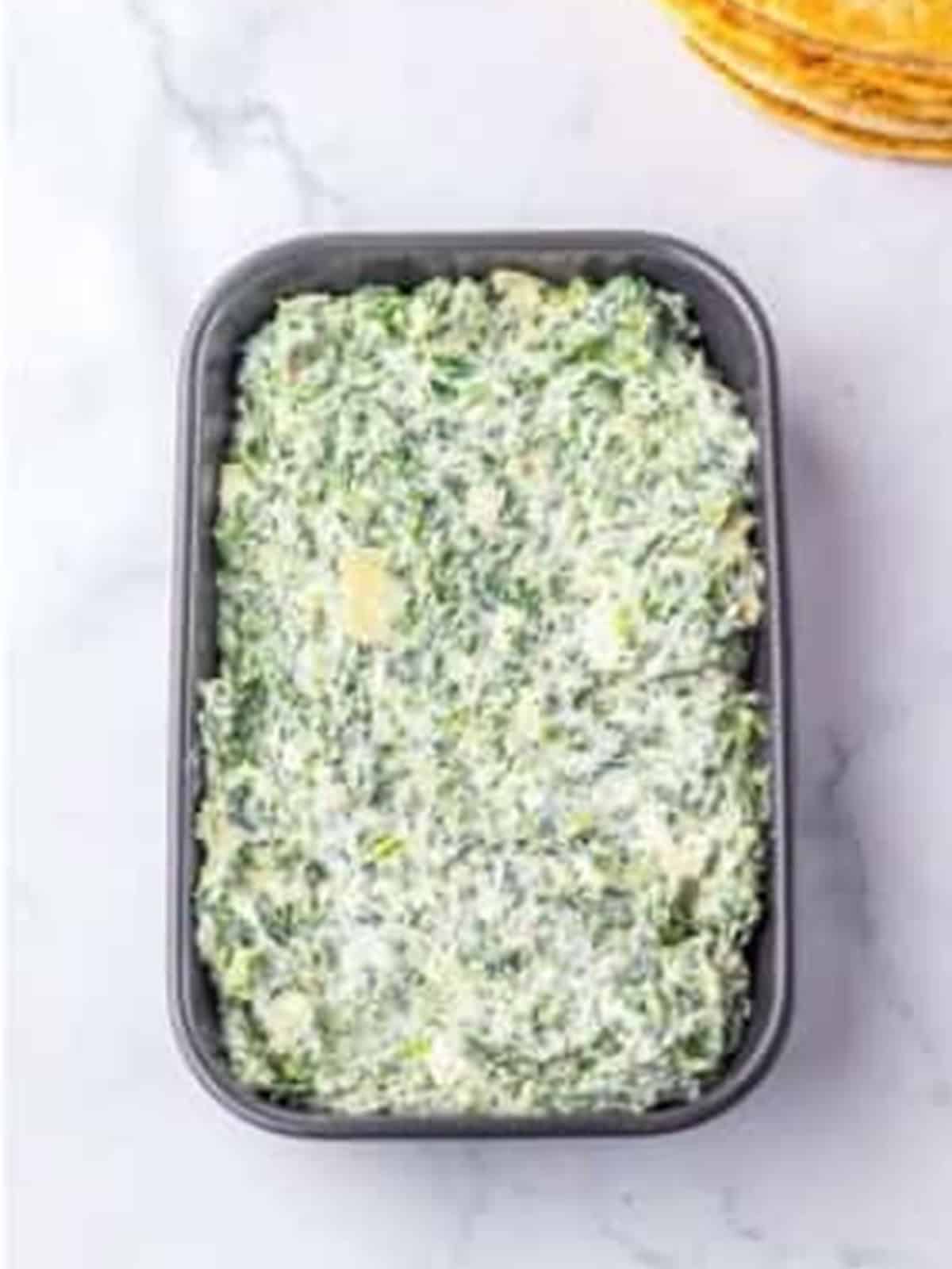 Spinach dip mixture spread into a baking dish.