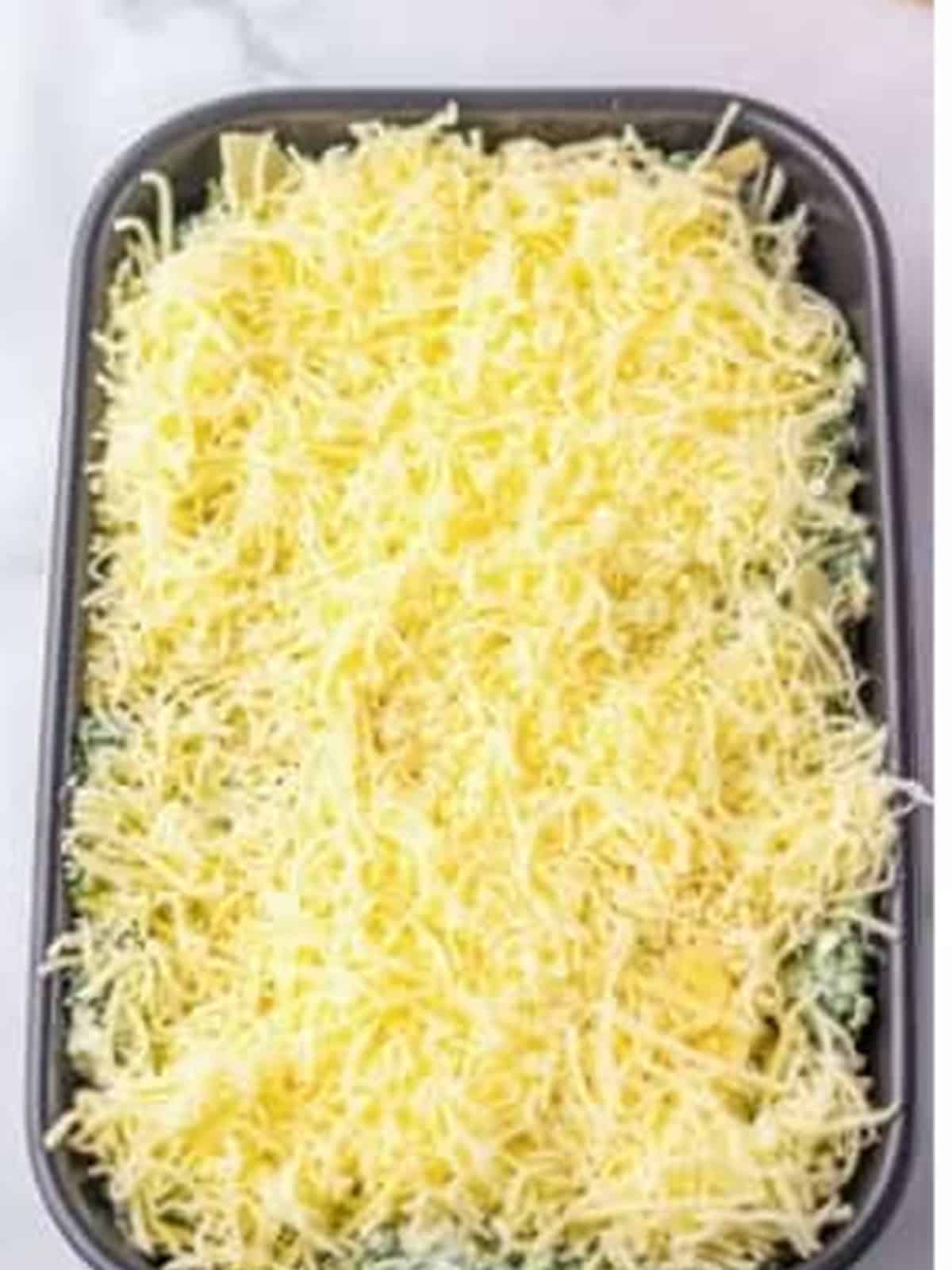 Spinach dip topped with shredded cheese before baking.