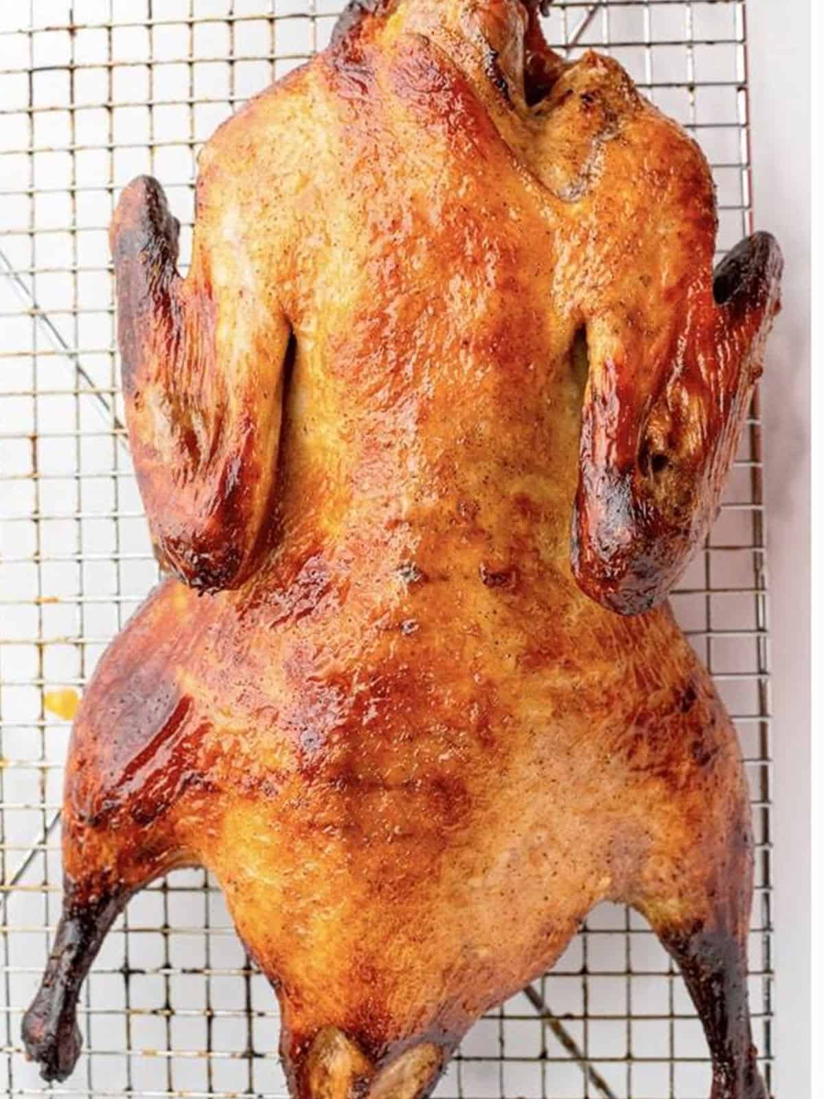 Roasted Peking duck with crispy mahogany skin resting on a wire rack.