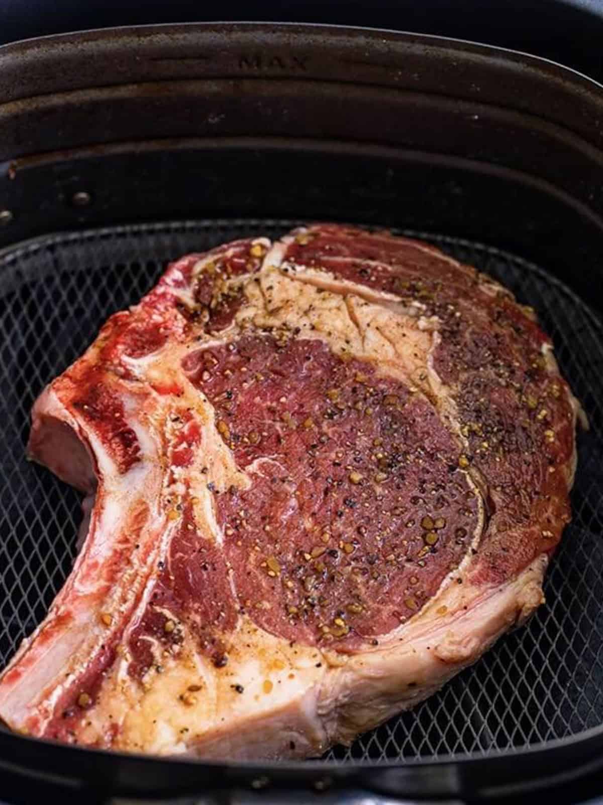 Marinated bone-in ribeye steak placed in the air fryer basket.