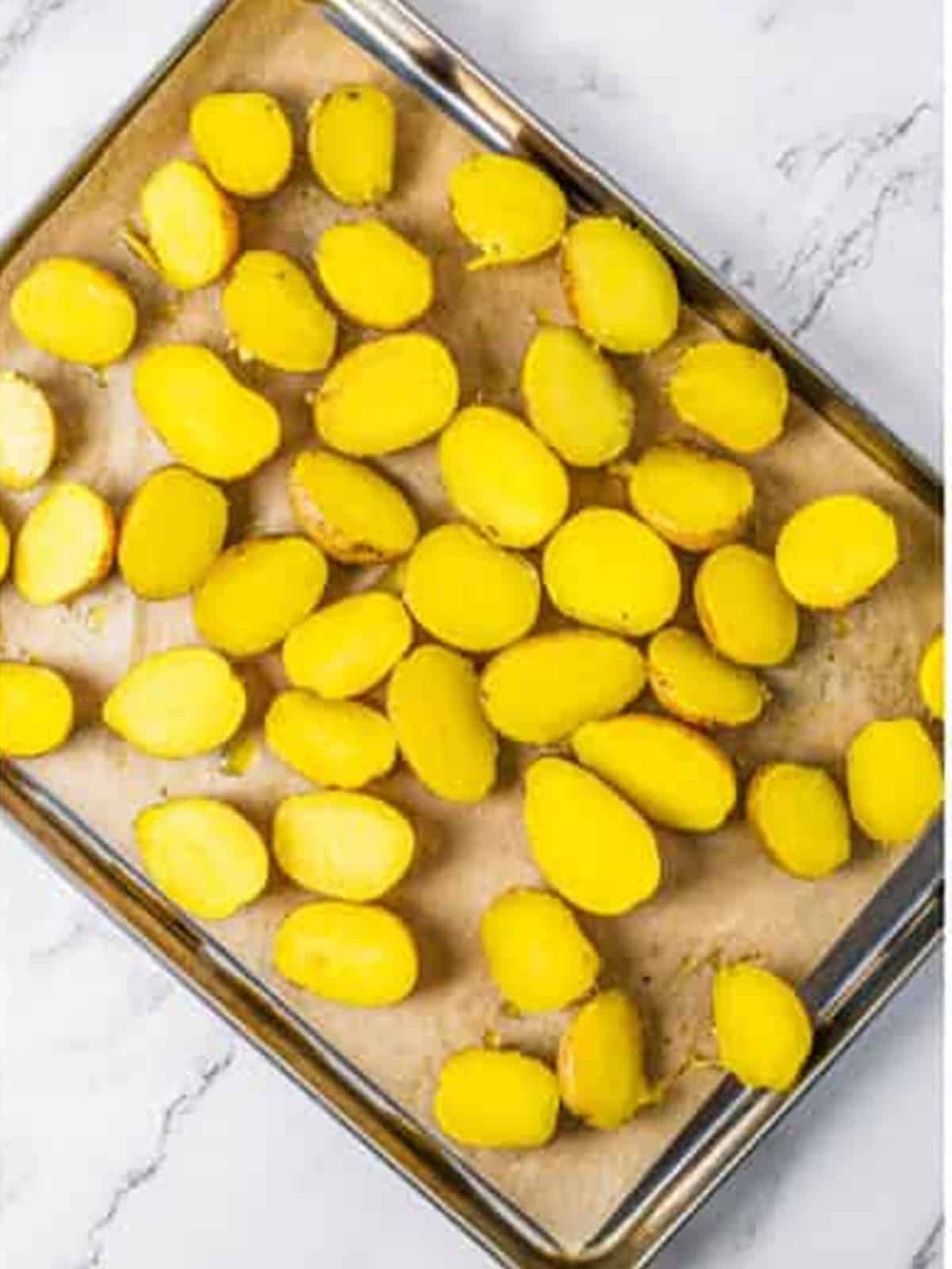Baby potatoes tossed with olive oil and seasoning in a baking dish before roasting.
