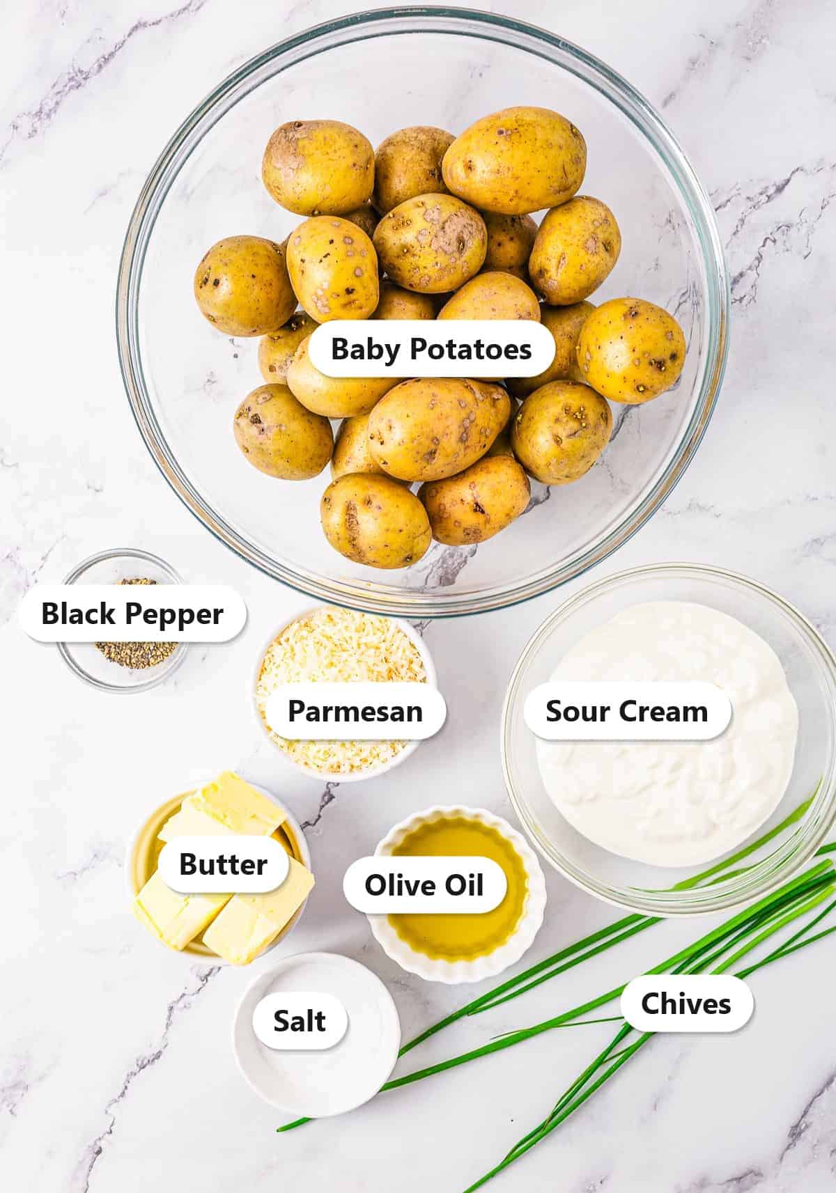 Labeled ingredients for parmesan potatoes including baby potatoes, parmesan, sour cream, butter, olive oil, chives, salt, and black pepper.
