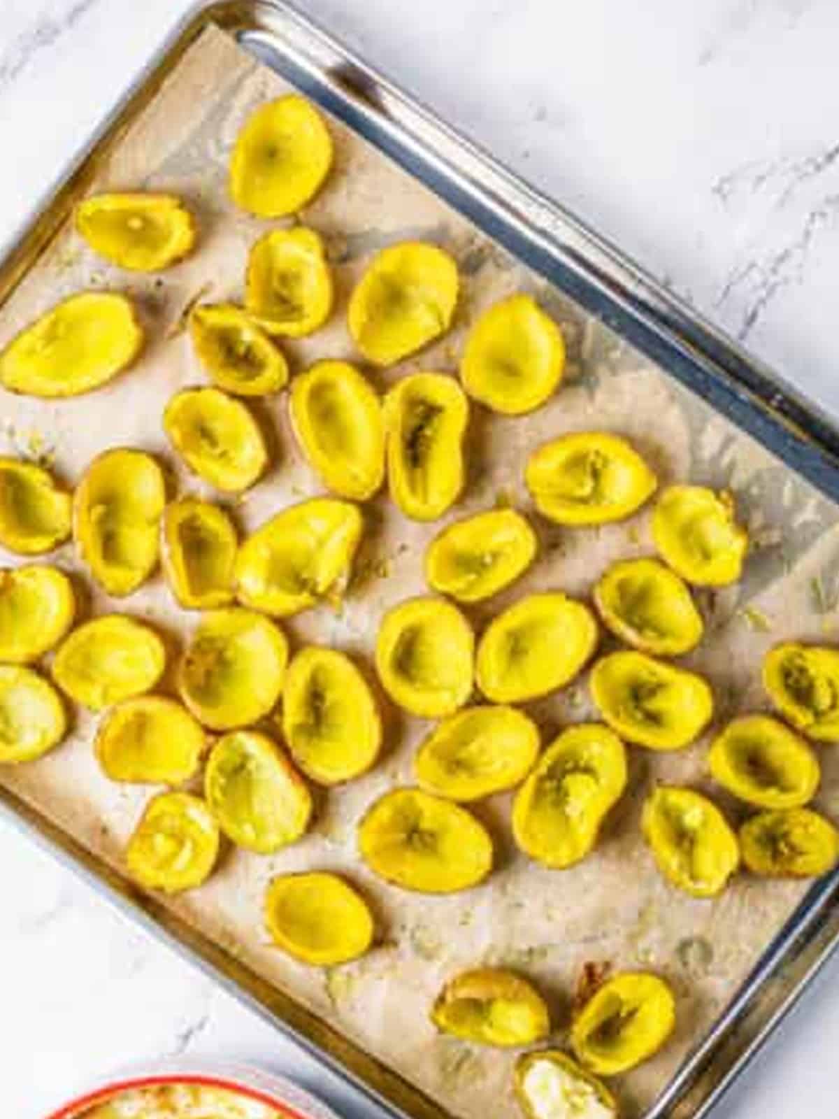 Baked potatoes halved and scooped into skins on a baking sheet.