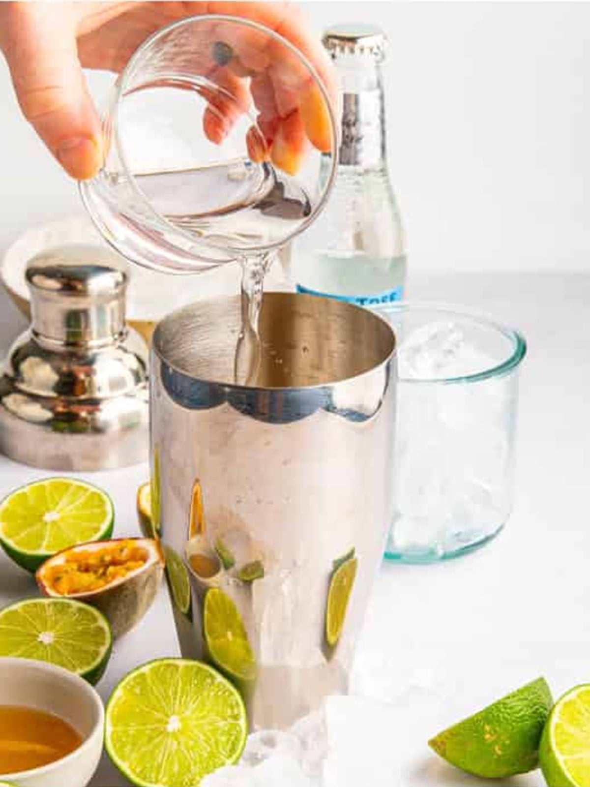 Pouring gin into a cocktail shaker for a passion fruit gin fizz.