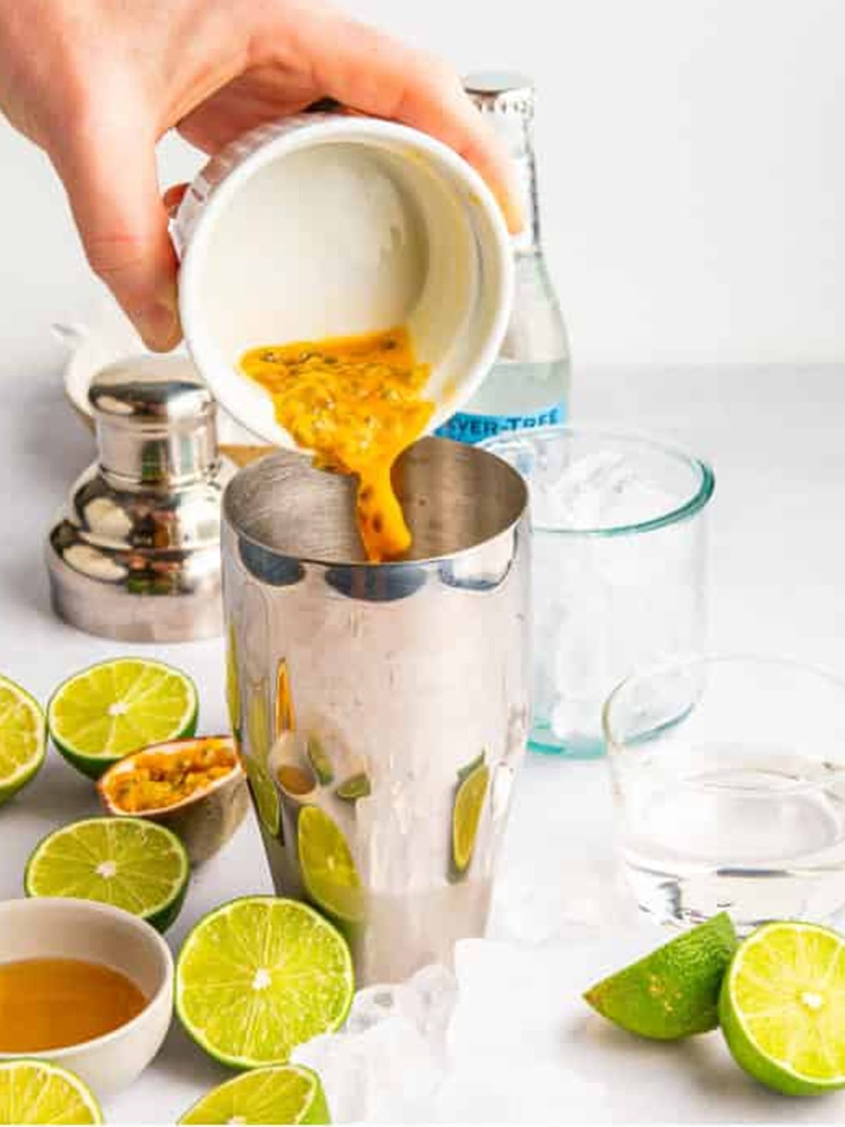 Adding passion fruit pulp to the shaker with gin and lime.