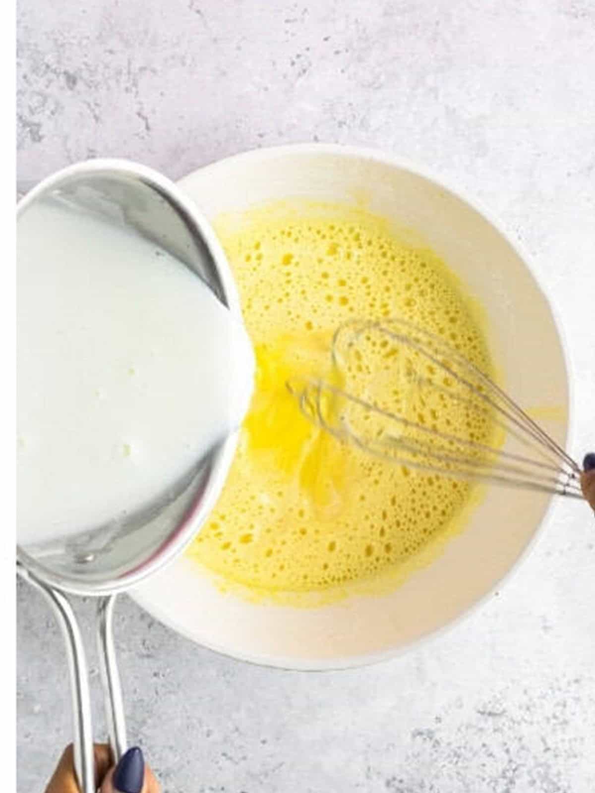 Tempering the eggs by drizzling in hot milk while whisking.