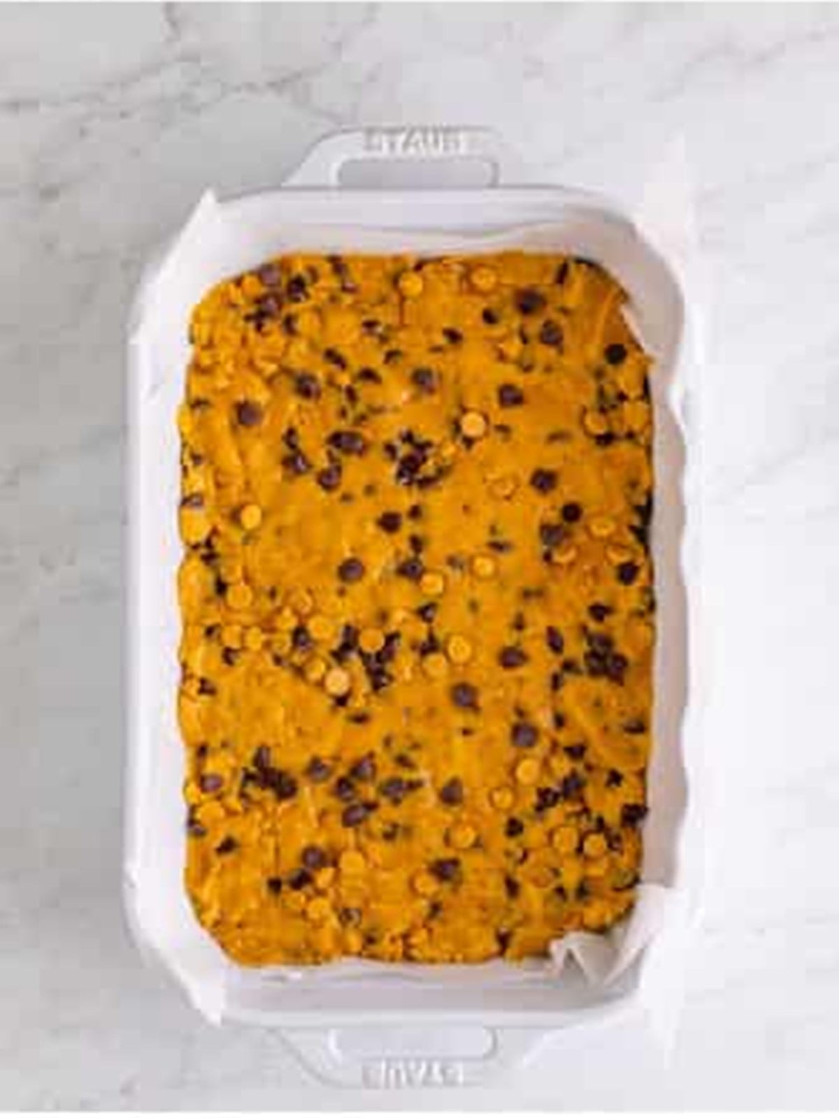 Cookie bar dough pressed into a parchment-lined pan ready to bake.