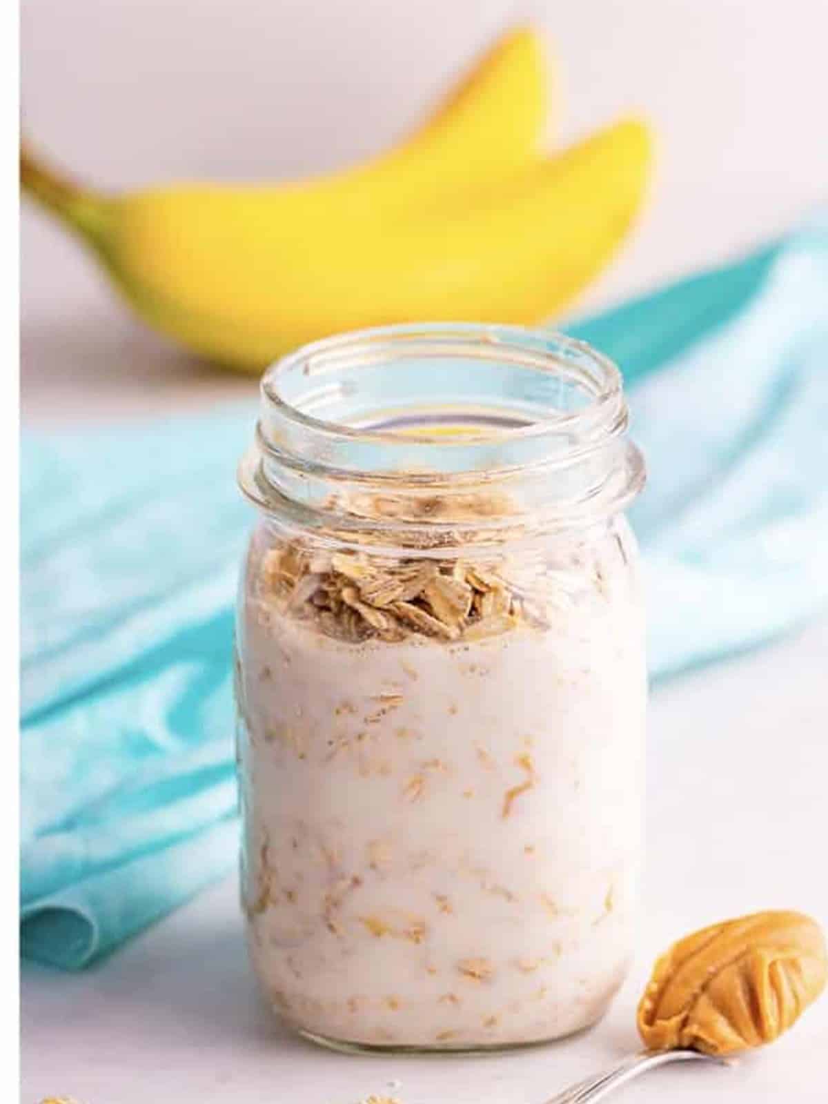 Rolled oats added on top of the peanut butter milk mixture in a jar.