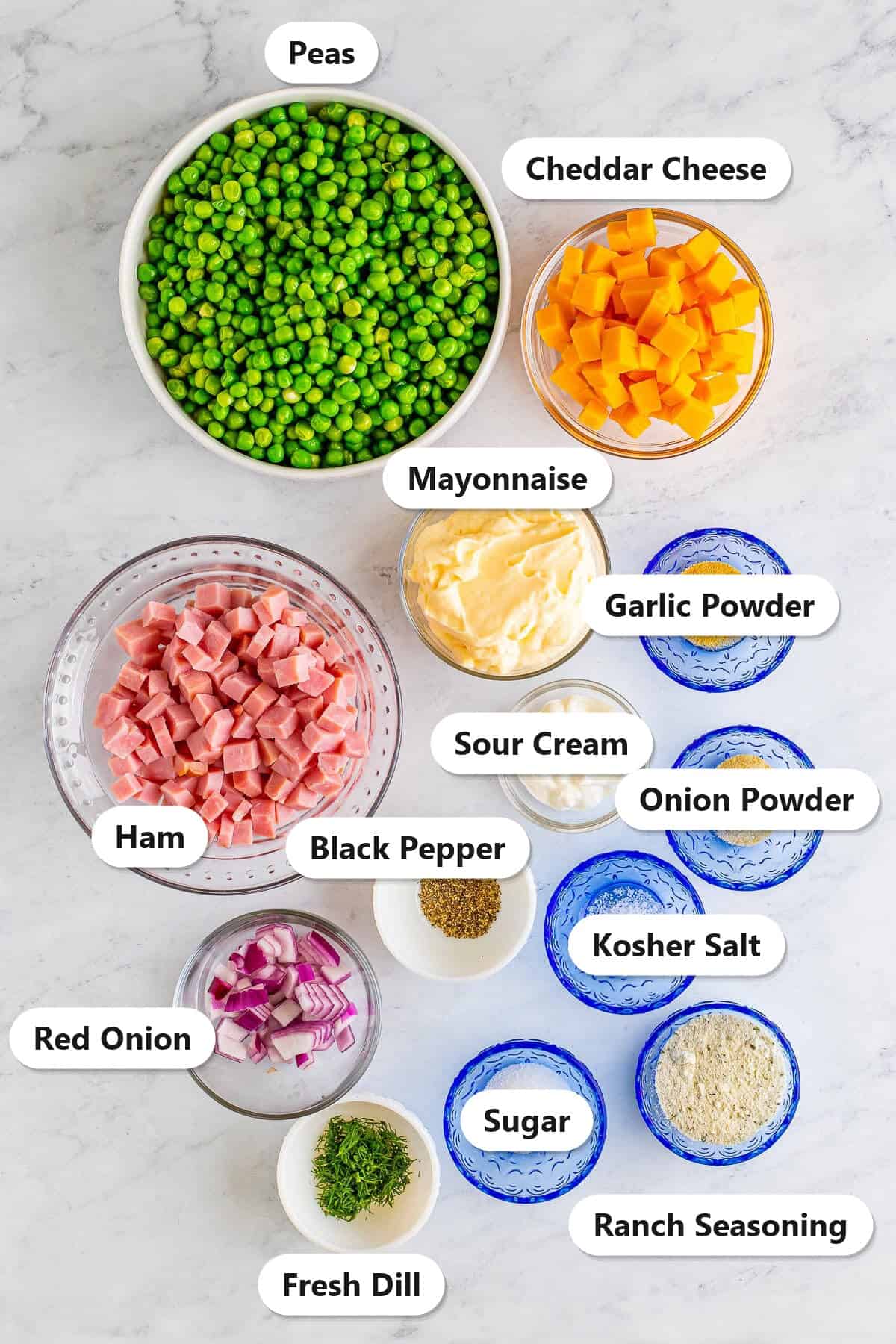 Labeled ingredients for pea salad including peas, cheddar cheese, ham, mayonnaise, sour cream, ranch seasoning, red onion, fresh dill, sugar, garlic powder, onion powder, kosher salt, and black pepper.