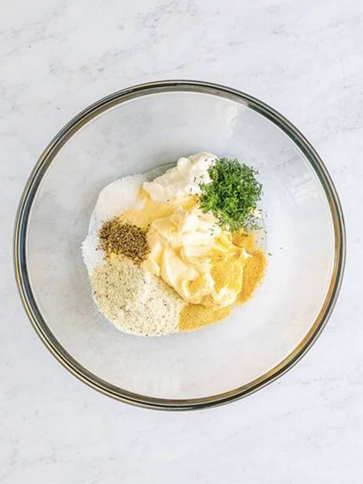 Mayonnaise, sour cream, ranch seasoning, dill, and seasonings added to a glass mixing bowl for pea salad dressing.