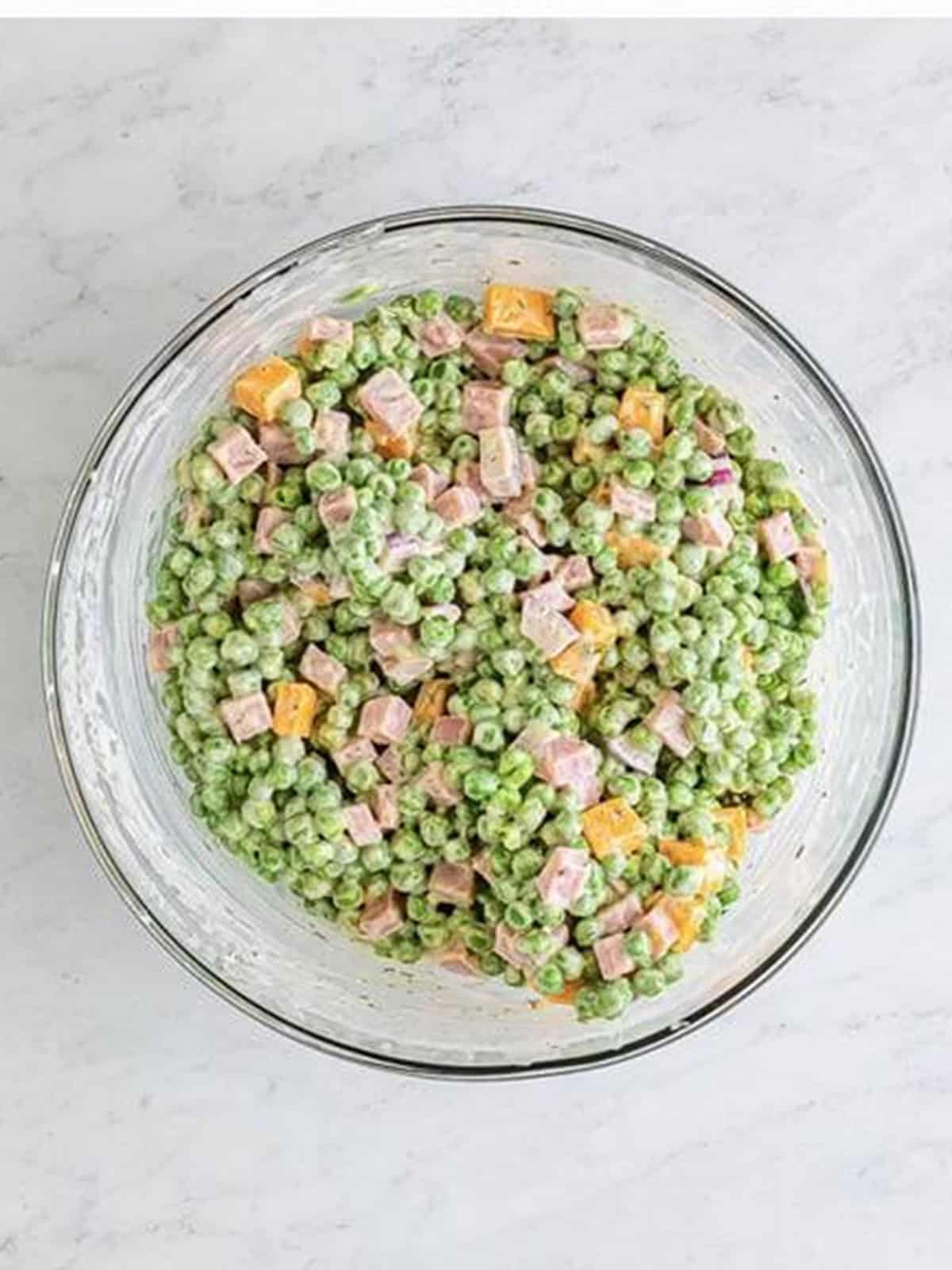 Pea salad stirred together so the peas, ham, and cheddar are coated in the creamy dressing.