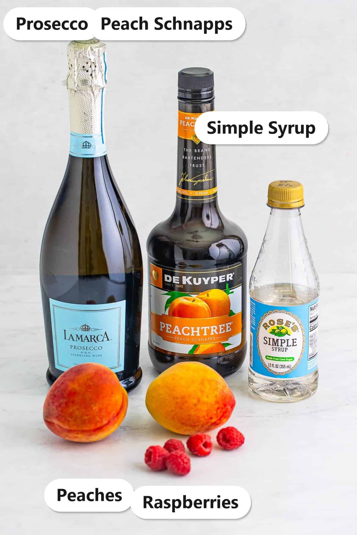 Labeled ingredients to make a peach bellini including Prosecco, peach schnapps, simple syrup, fresh peaches, and raspberries.