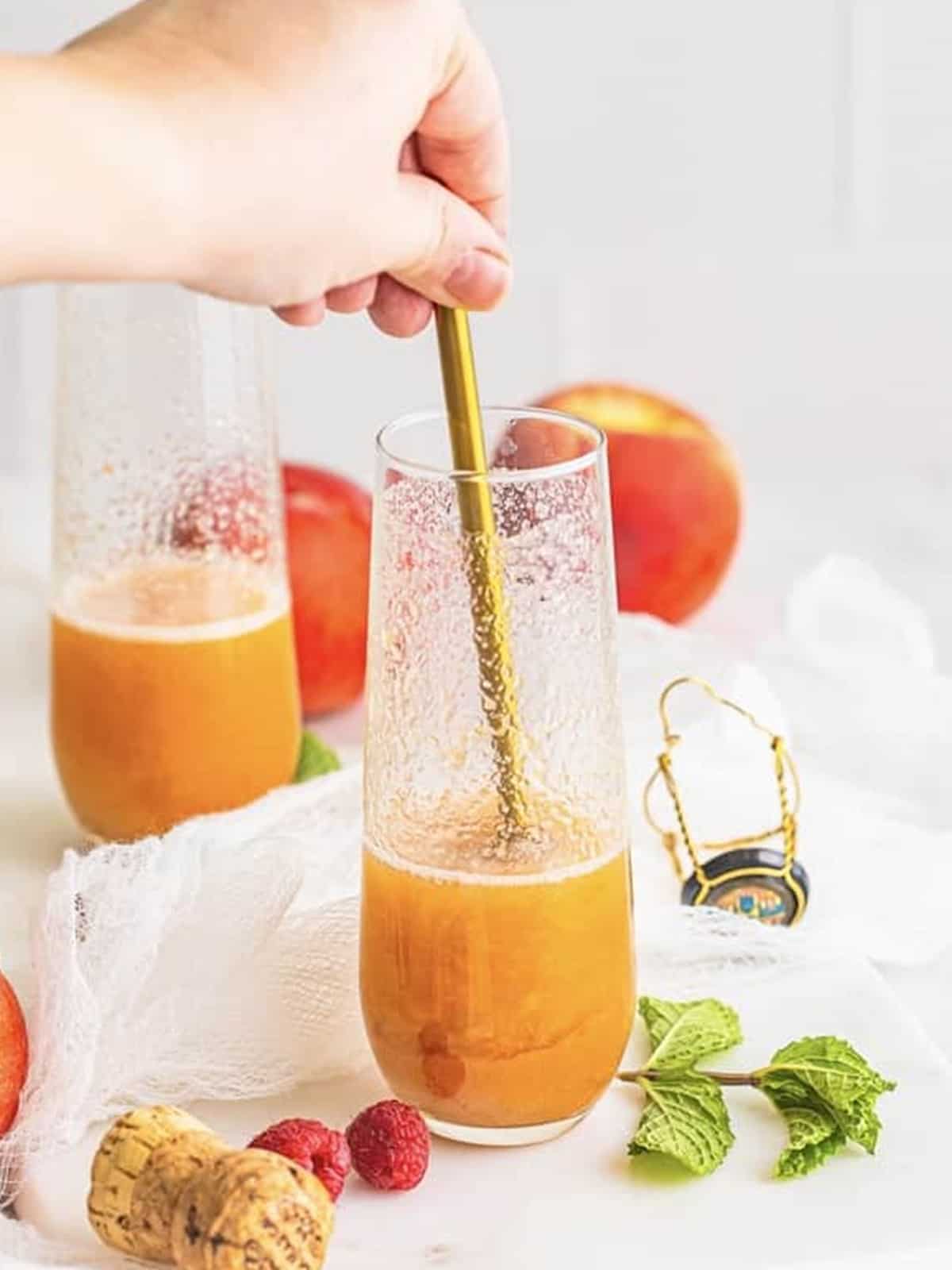 Gently stirring a peach bellini in a champagne flute.