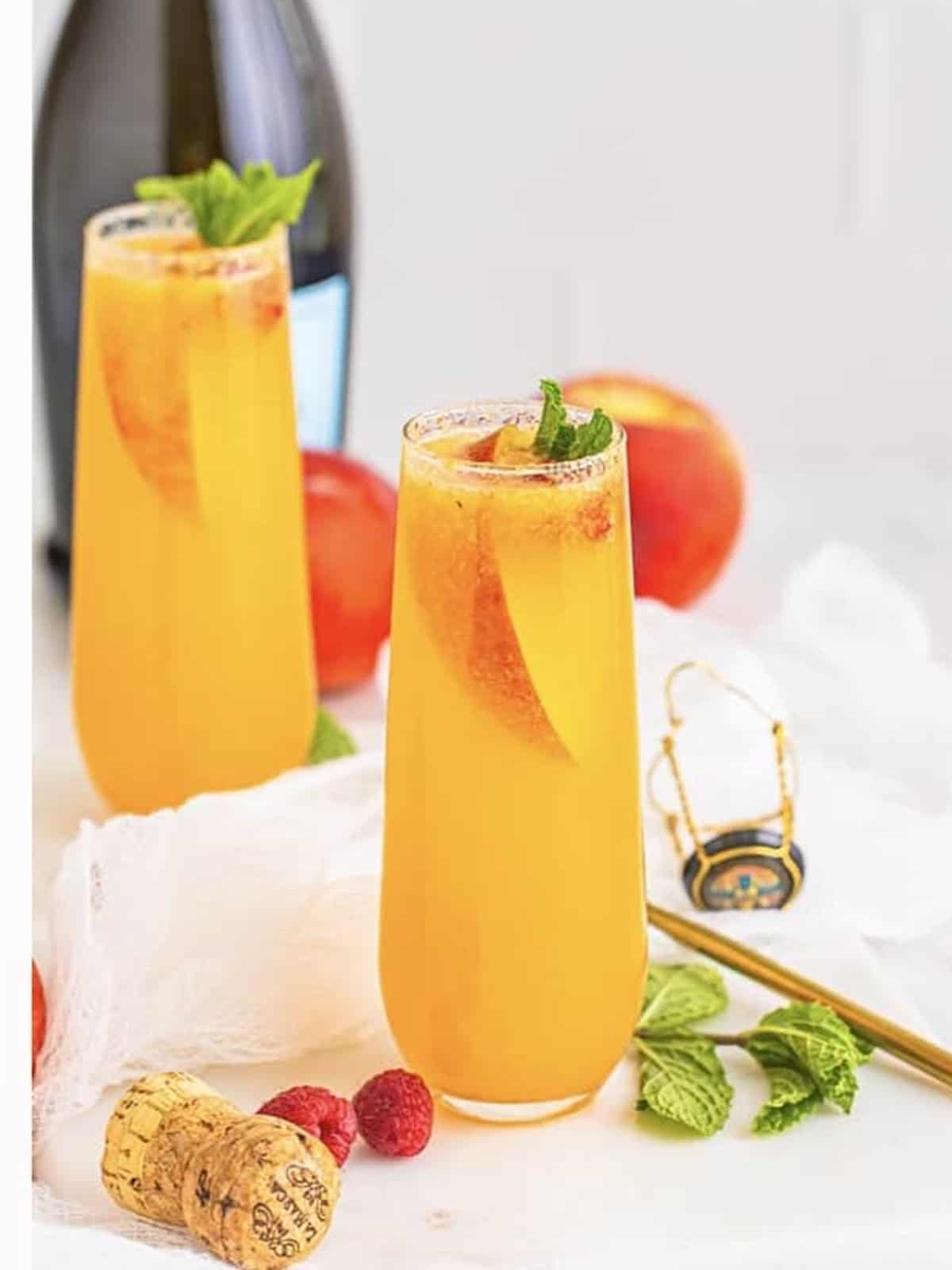 Finished peach bellini cocktails garnished with peach slices, raspberries, and mint.