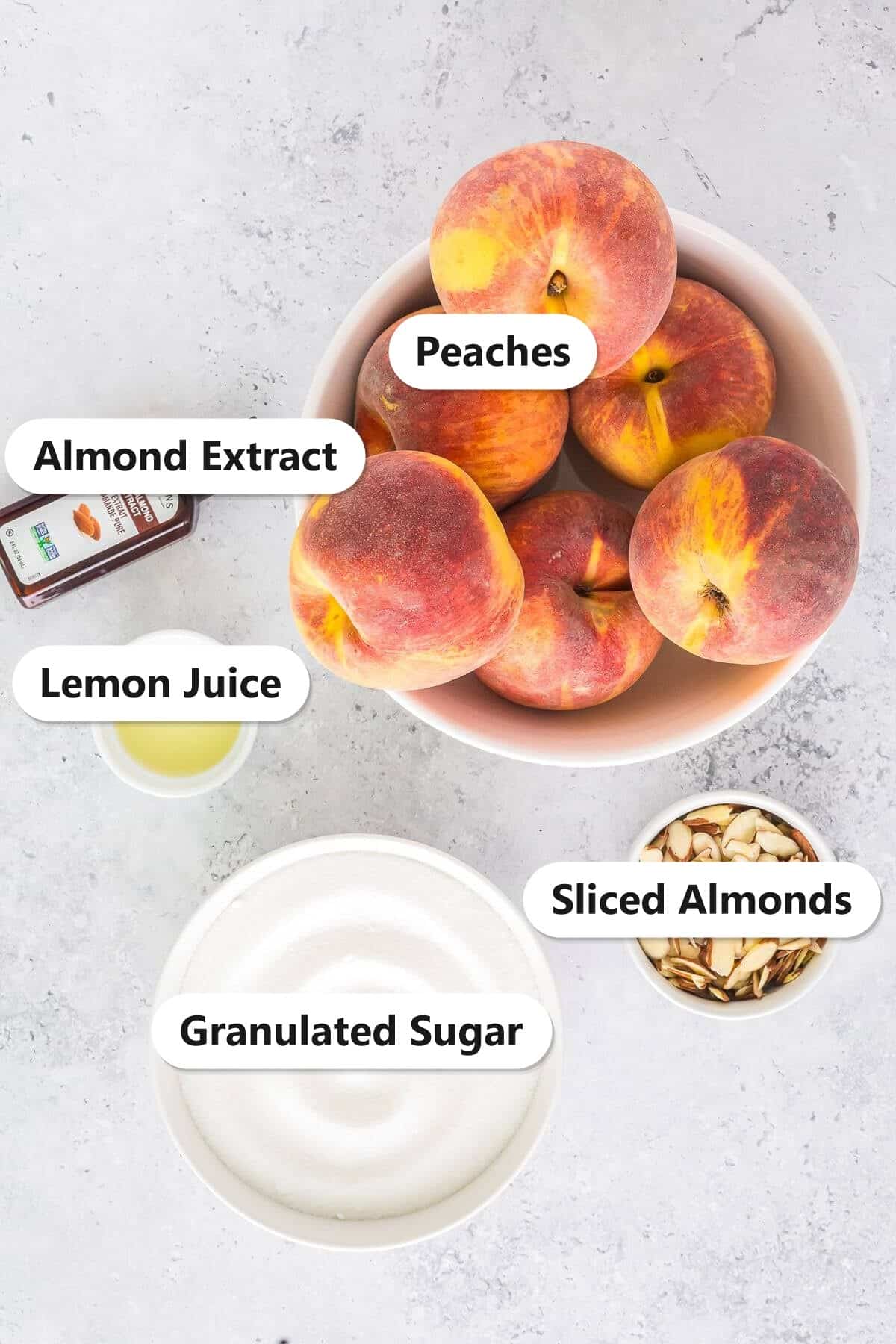 Peach jam ingredients including fresh peaches, granulated sugar, lemon juice, almond extract, and sliced almonds labeled on a marble surface.