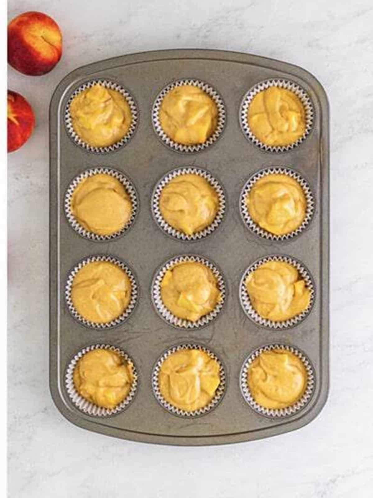 Peach muffin batter divided into a lined muffin tin.