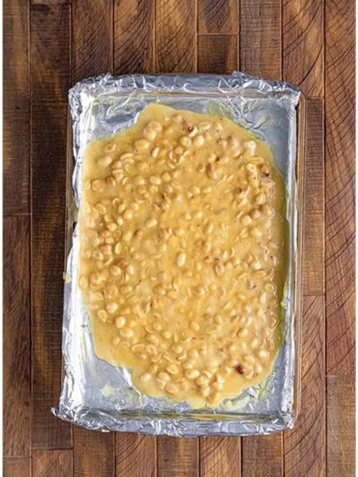 The peanut brittle spread in a thin layer on a foil lined tray.