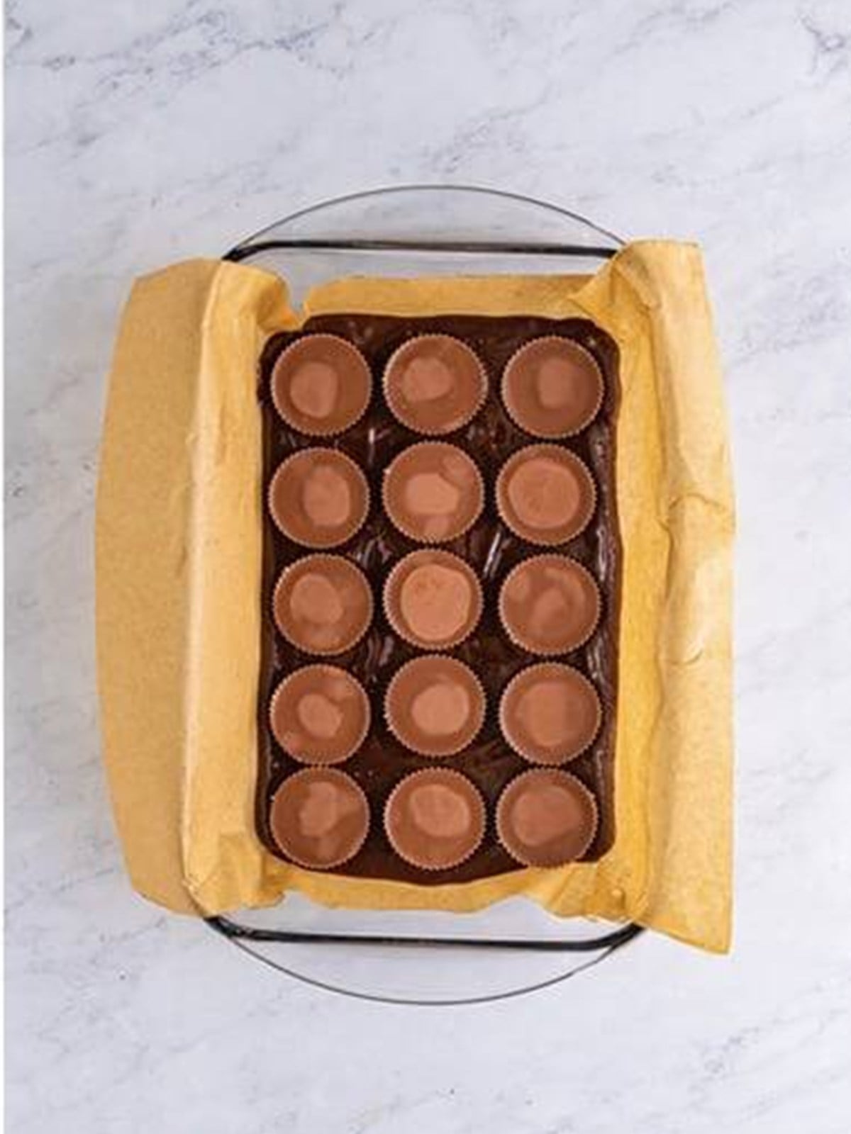Peanut butter cups pressed into brownie batter in a parchment lined pan.