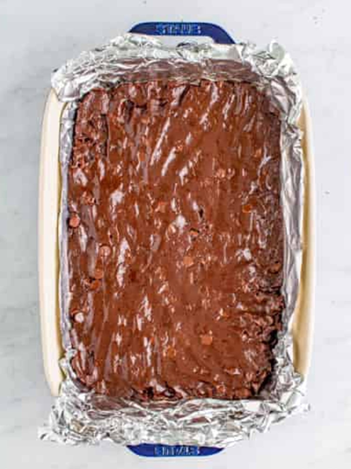 Brownie batter pressed into a foil-lined baking dish before baking.