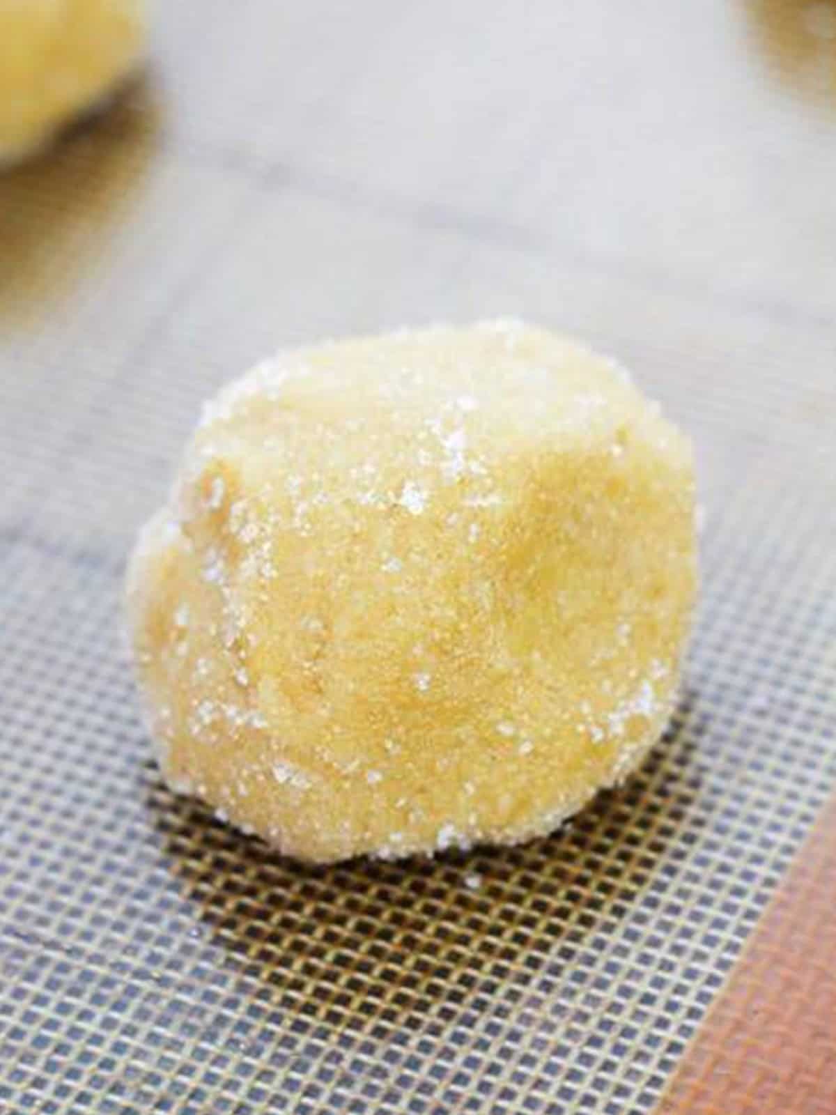 Sugar coated cookie dough balls on a lined baking sheet.
