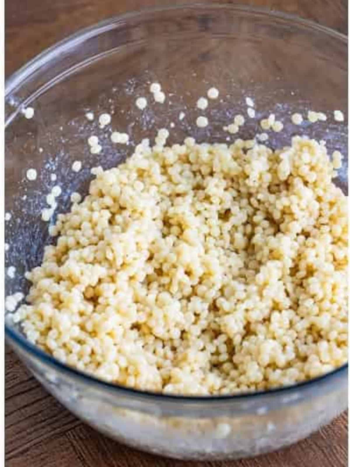 Cooked pearl couscous cooling to room temperature in a large glass bowl.