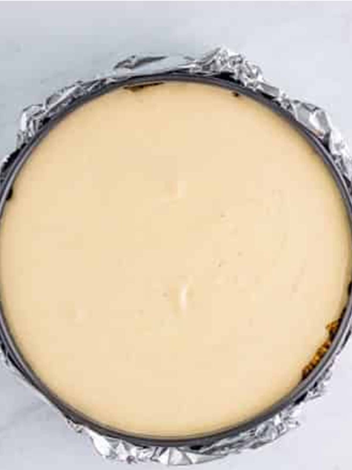Pecan pie cheesecake batter poured into a foil-wrapped springform pan for a water bath.