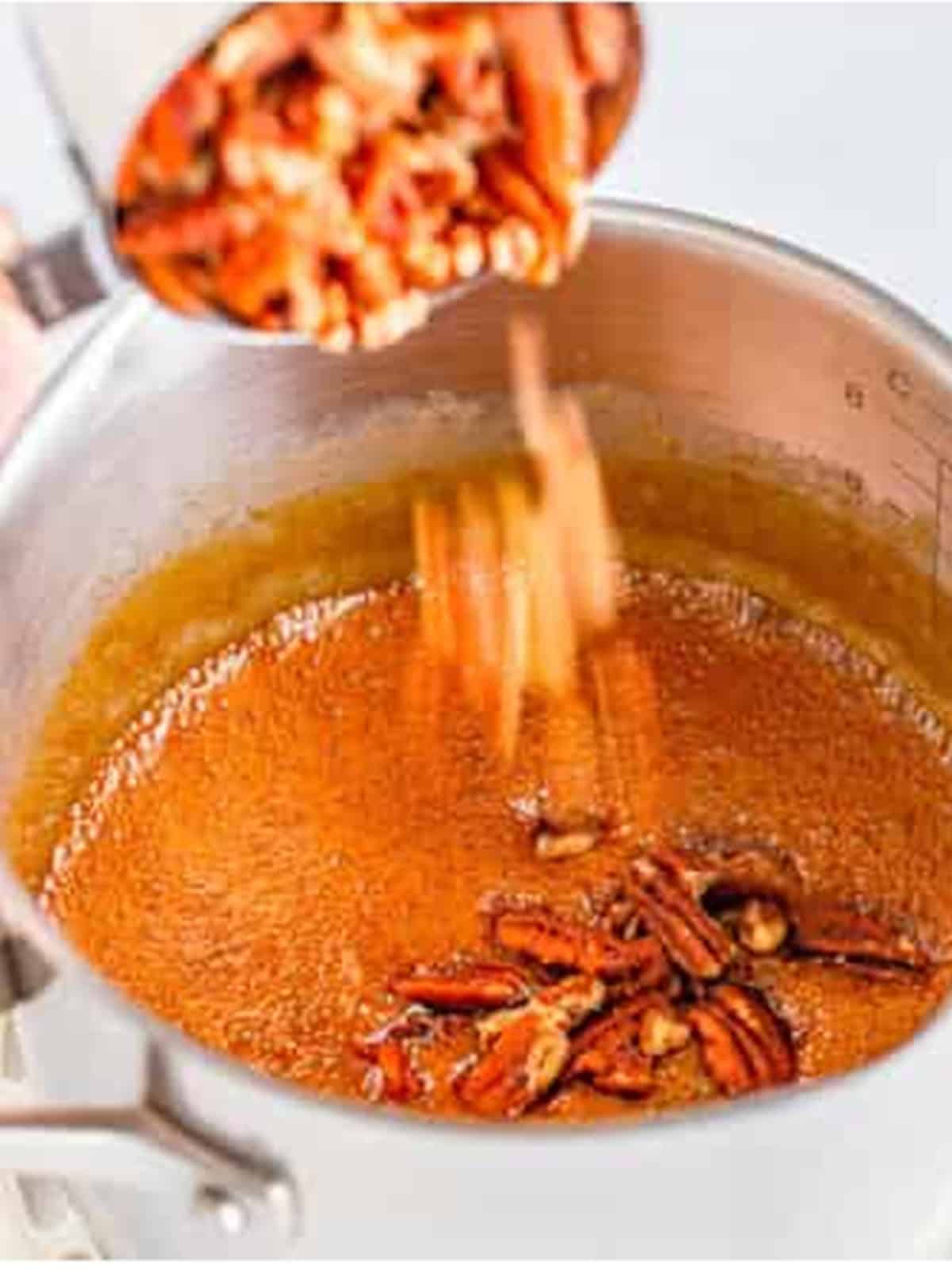 Chopped pecans stirred into the bubbling caramel pecan pie topping in a saucepan.