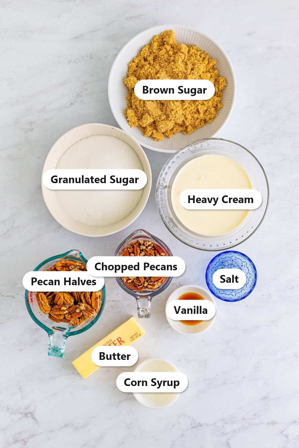 Labeled ingredients for pecan pralines including brown sugar, granulated sugar, heavy cream, pecan halves, chopped pecans, butter, corn syrup, vanilla, and salt.