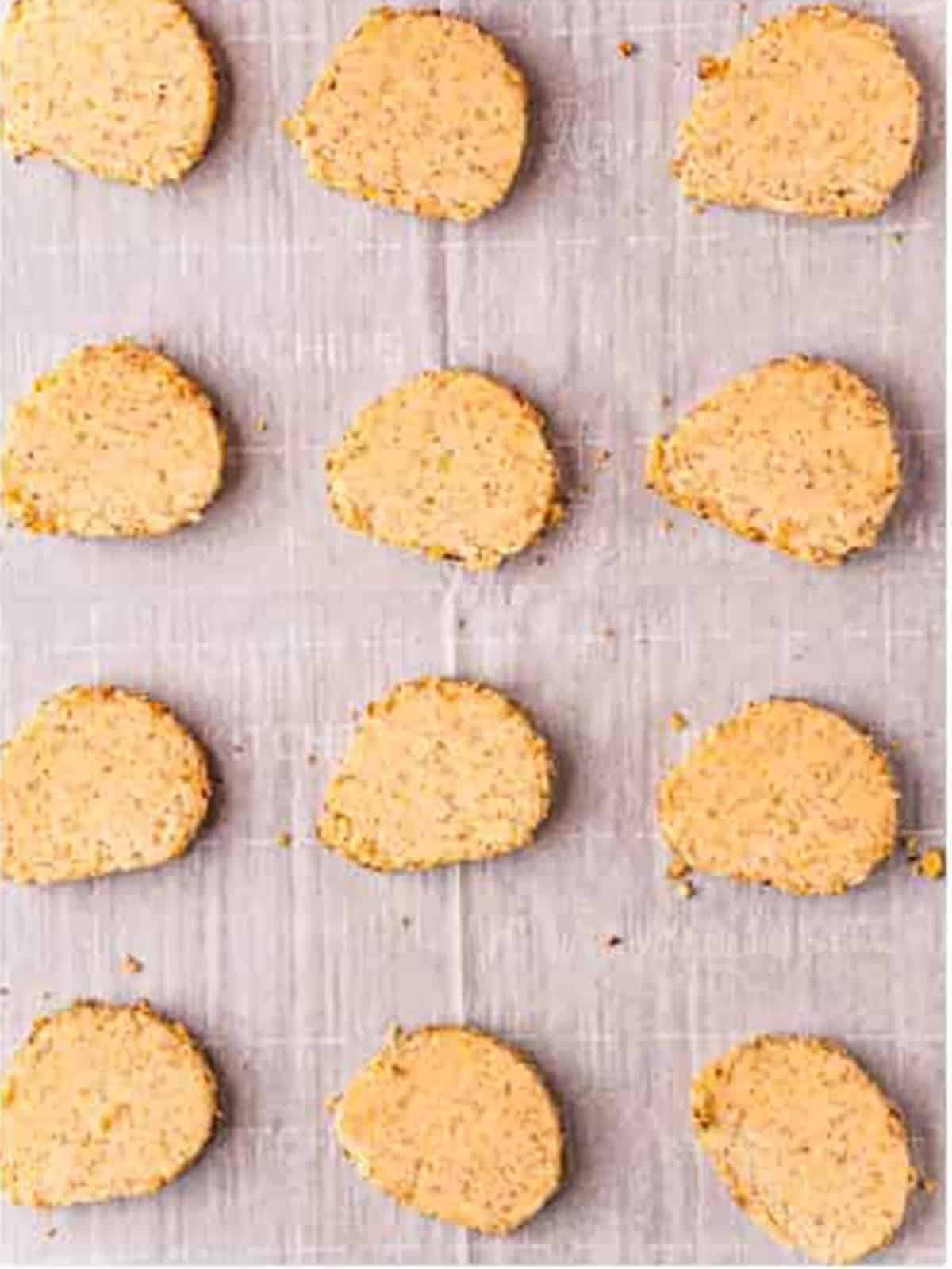 Sliced pecan sandies arranged on a parchment lined baking sheet ready to bake.