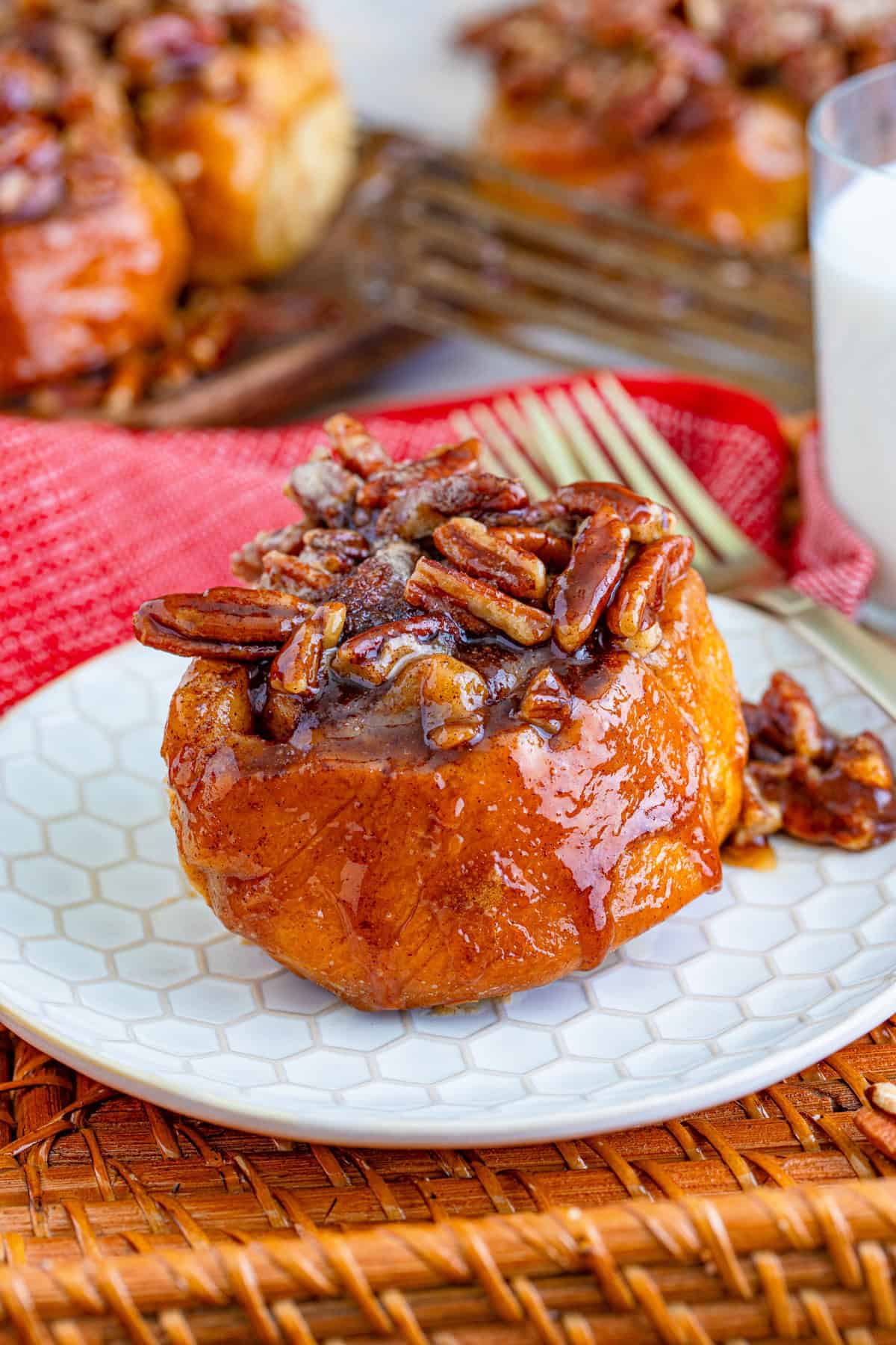 A single pecan sticky bun on a white plate dripping with caramel pecan topping.